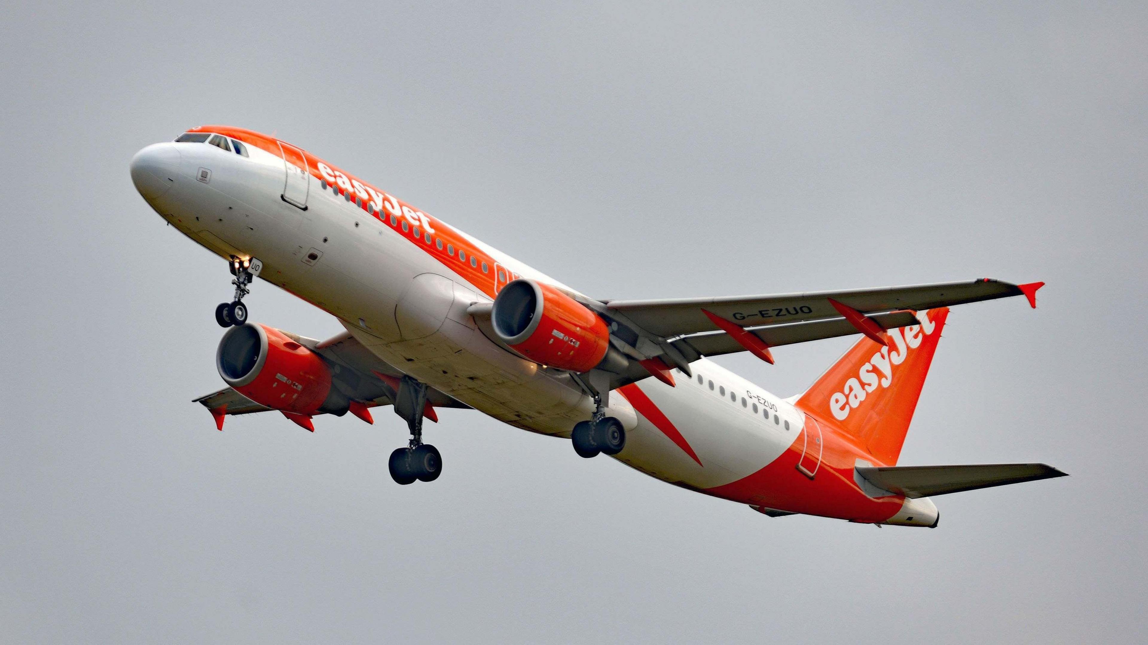 An Easyjet Airbus A320-214 passenger airliner coming in to land. The sky is cloudy and grey contrasting with the bright orange of Easyjet's colours.