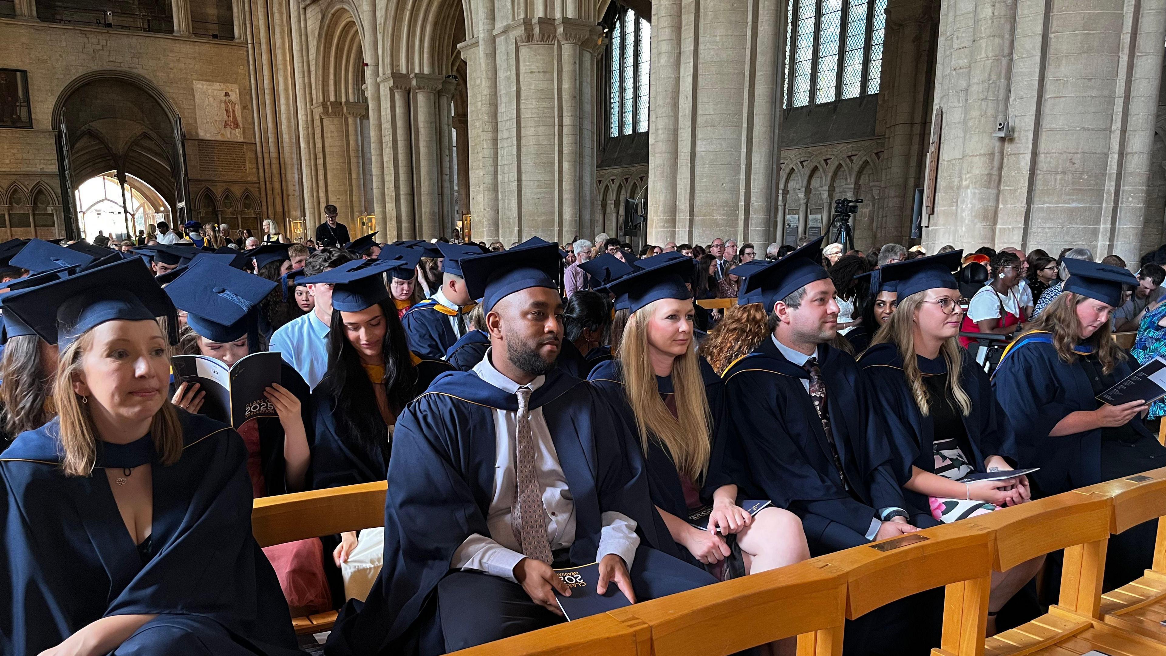 Rows of students in graduation caps and gowns sitting in Peterborough Cathedral.