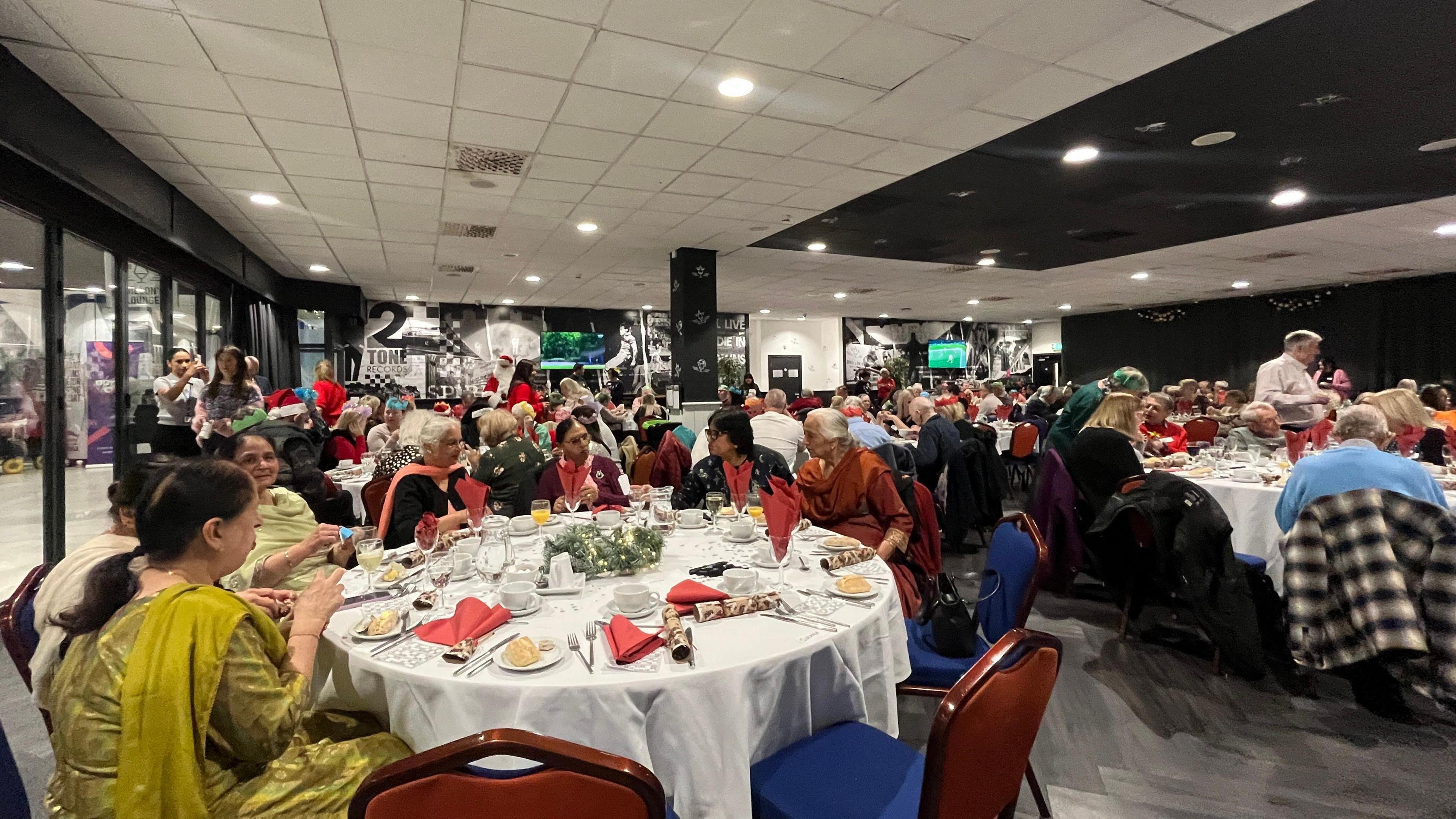 Guests are sitting at round tables with white cloths eating a Christmas dinner.