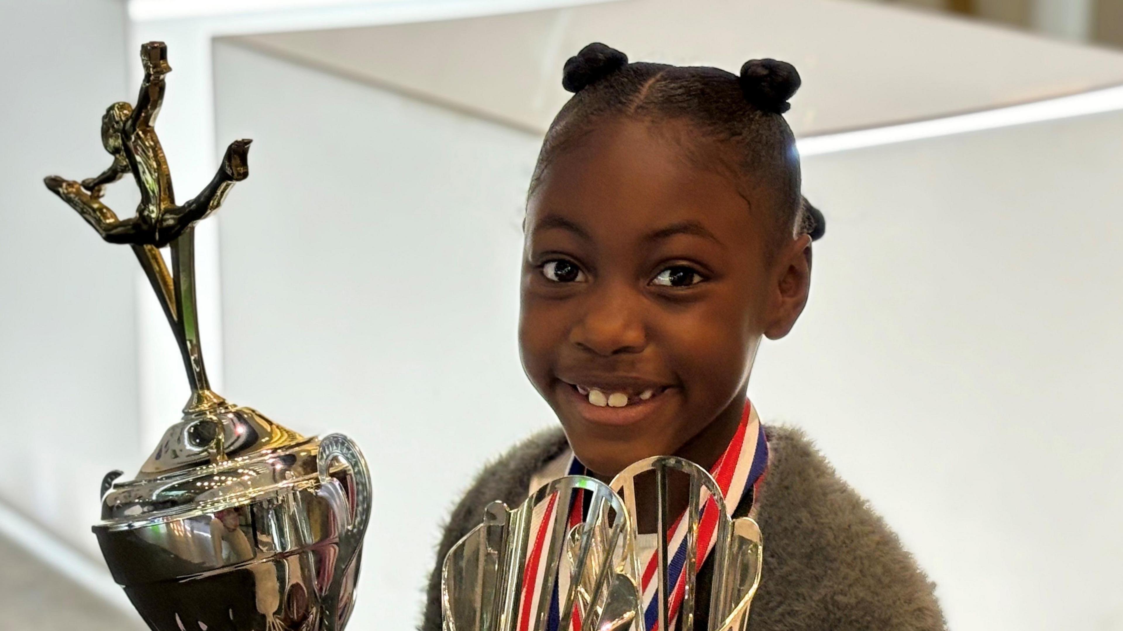 Lauren Larbi wearing medals and holding two gymnastics trop