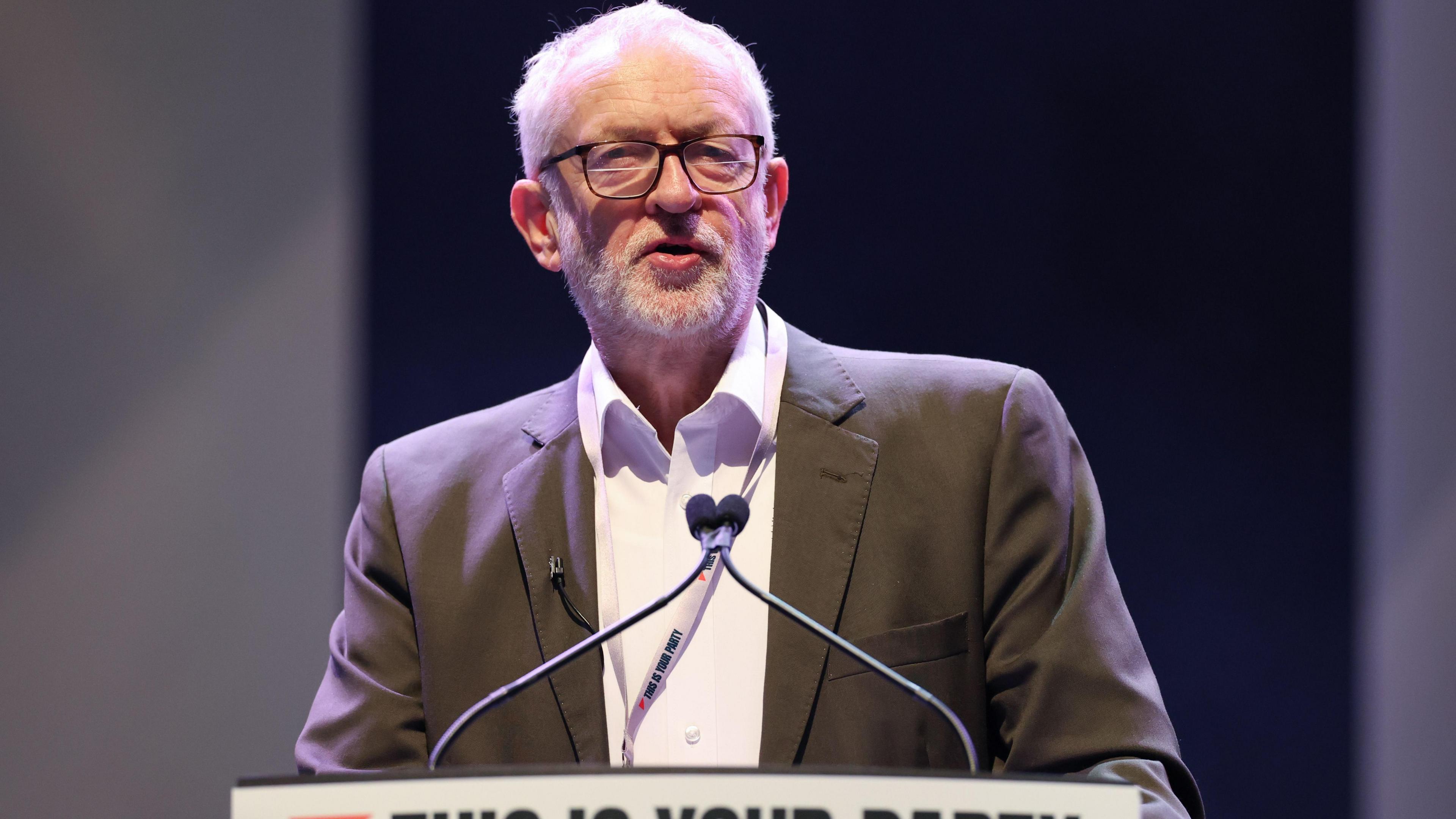 Jeremy Corbyn wearing a suit and shirt stands at a lectern addressing delegates during the Your Party conference in Liverpool