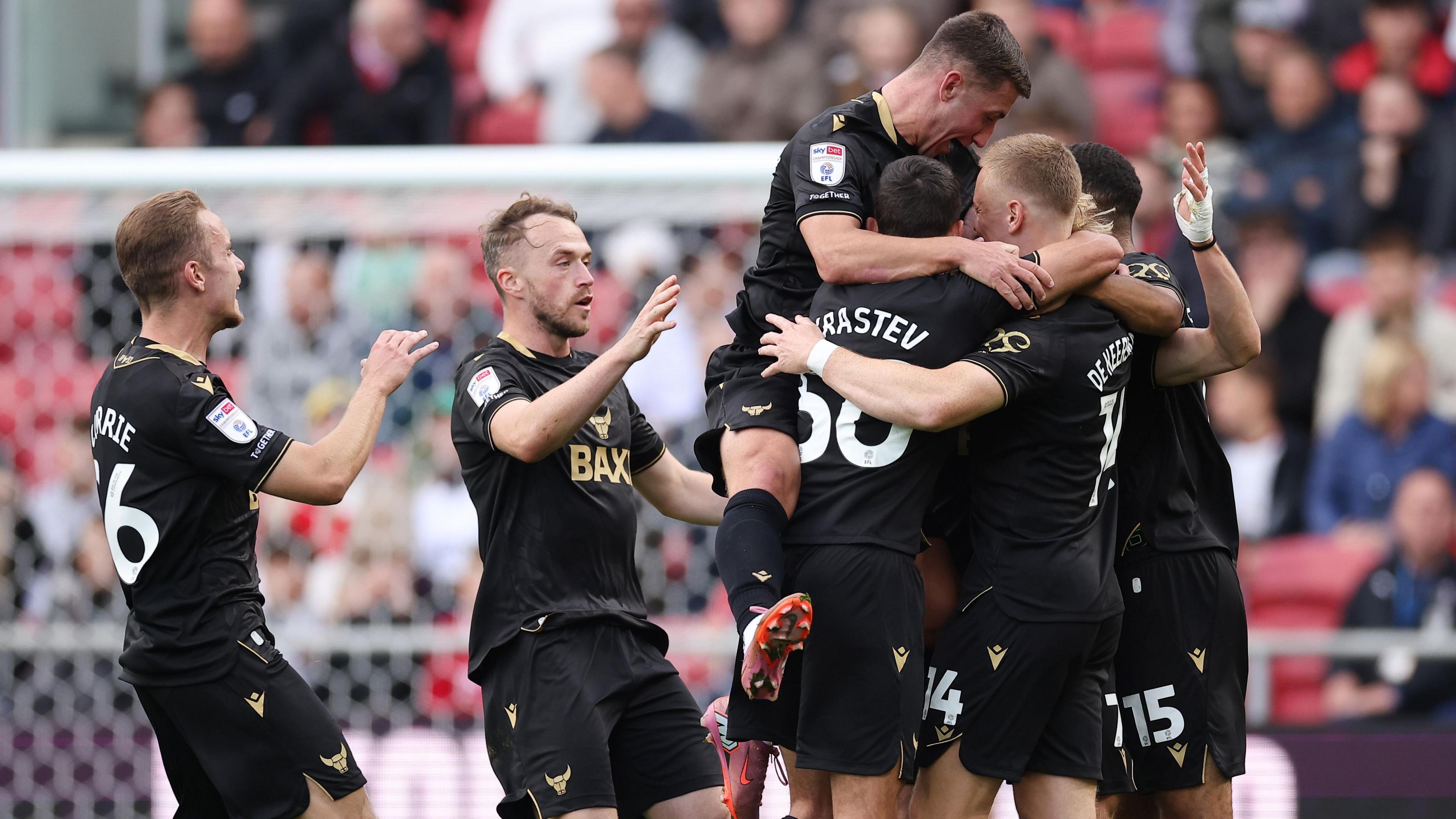 Oxford United players jump on each other and huddle together in celebration of a goal
