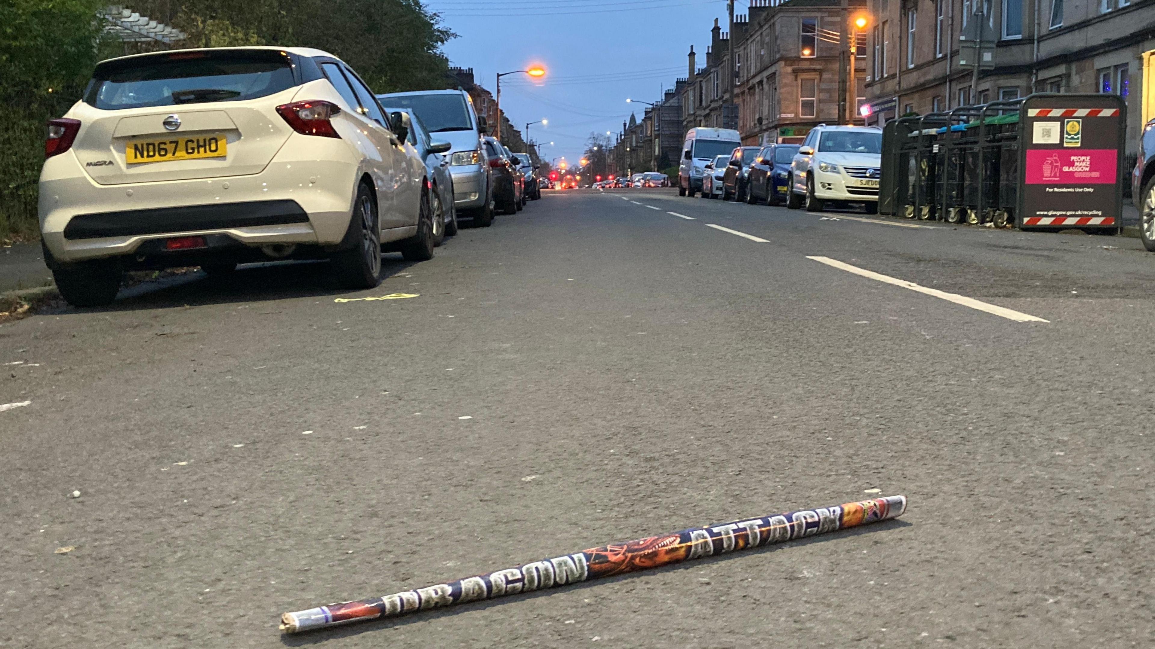 a large discarded firework lying in the middle of a road with cars parked on either side of the street