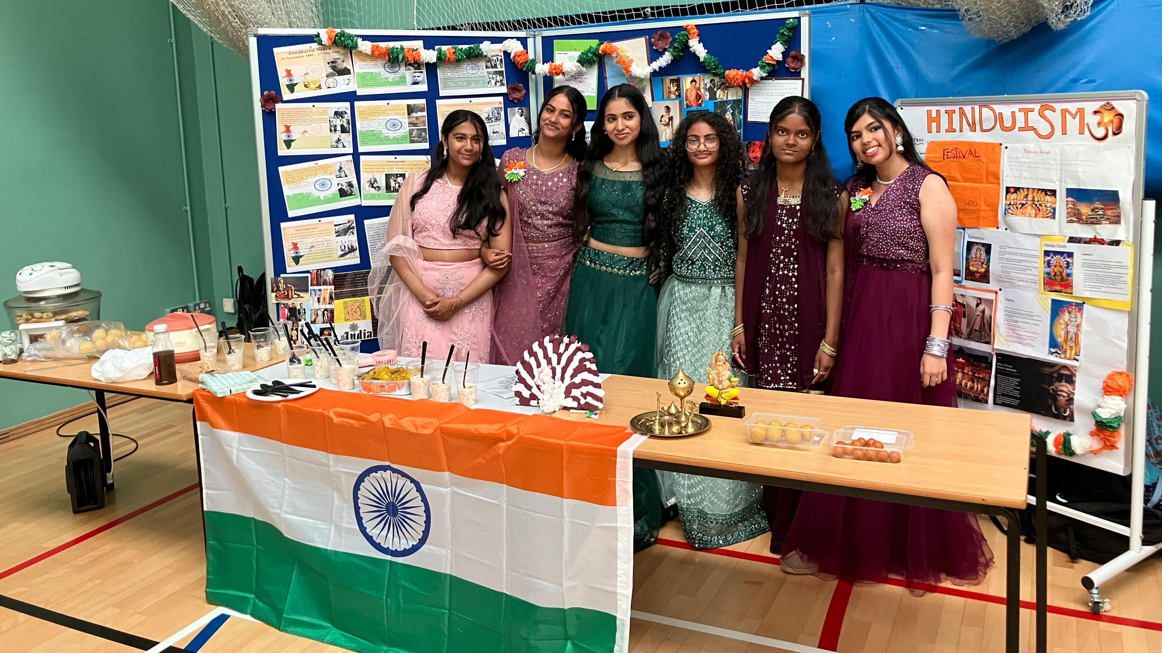 Six girls dressed in traditional Indian outfits standing in front of a display on India