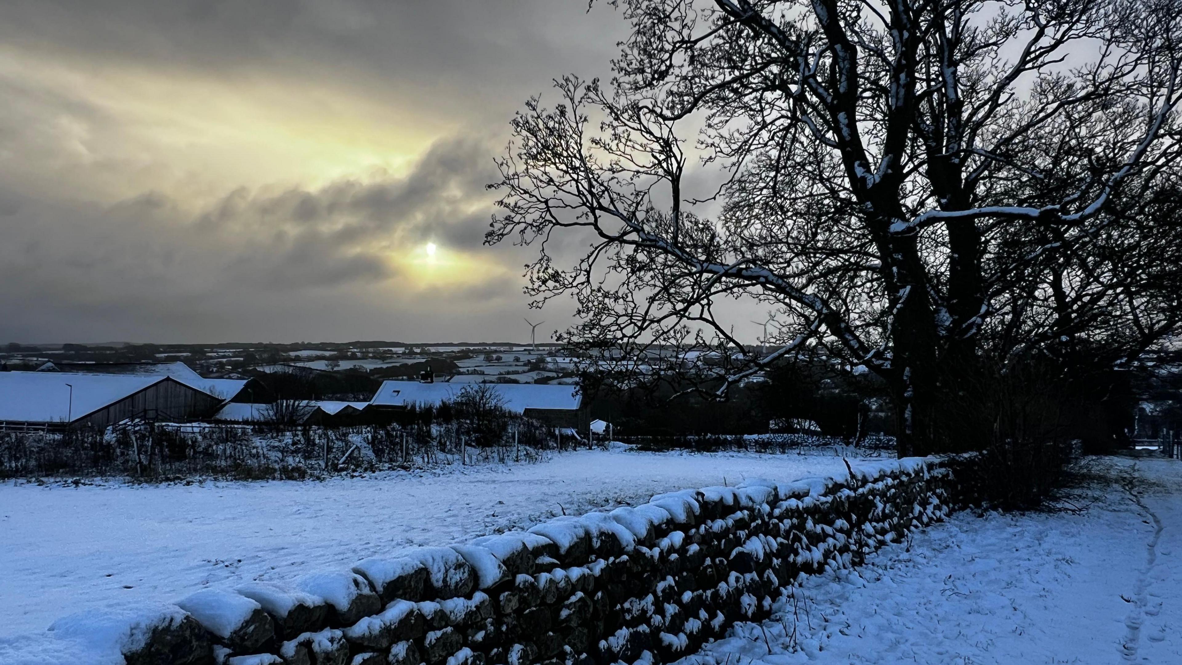 A rural scene at dawn of a dark sky with snow on the ground