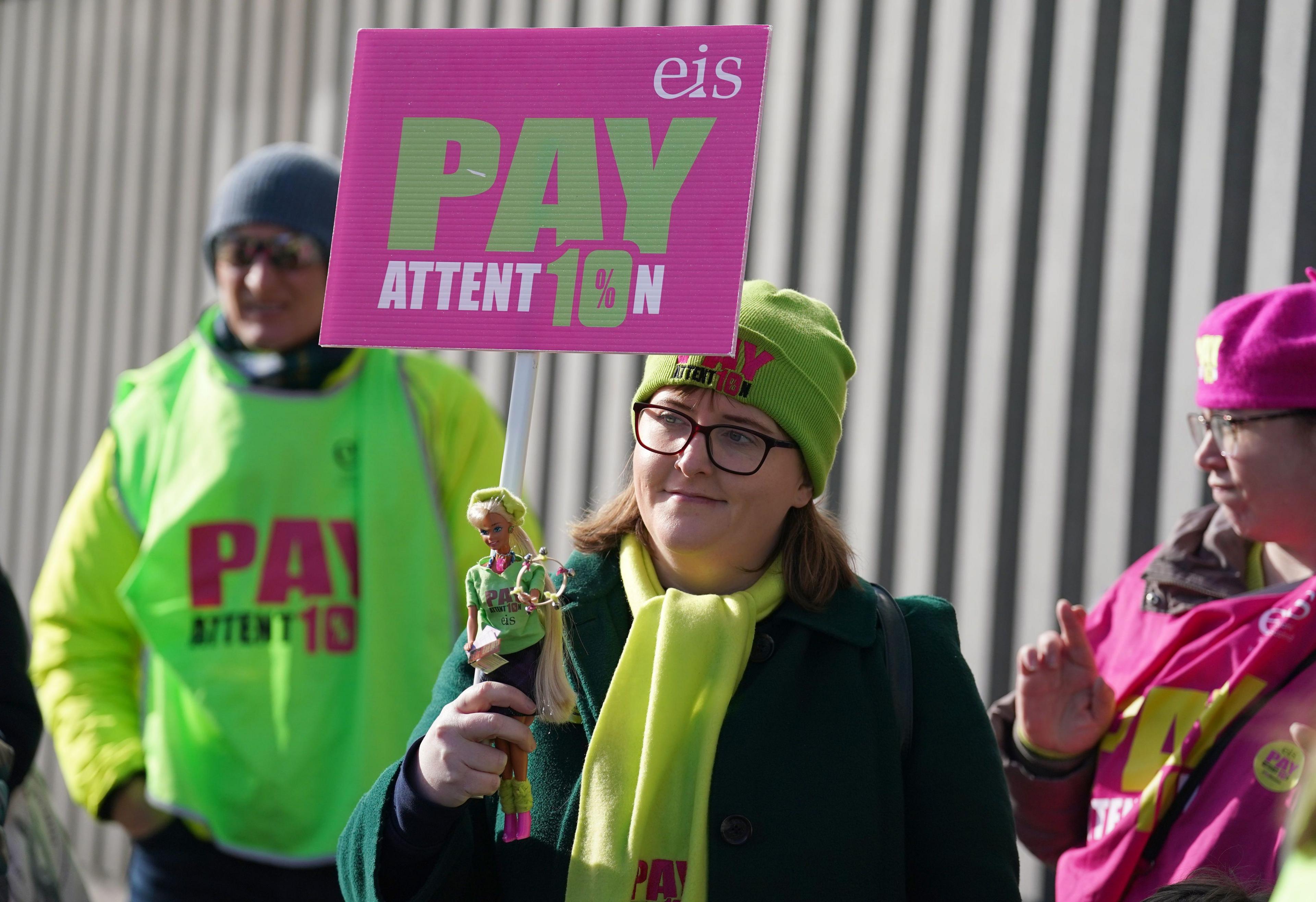 A female EIS member holding a pink and green placard which says "Pay Attention".