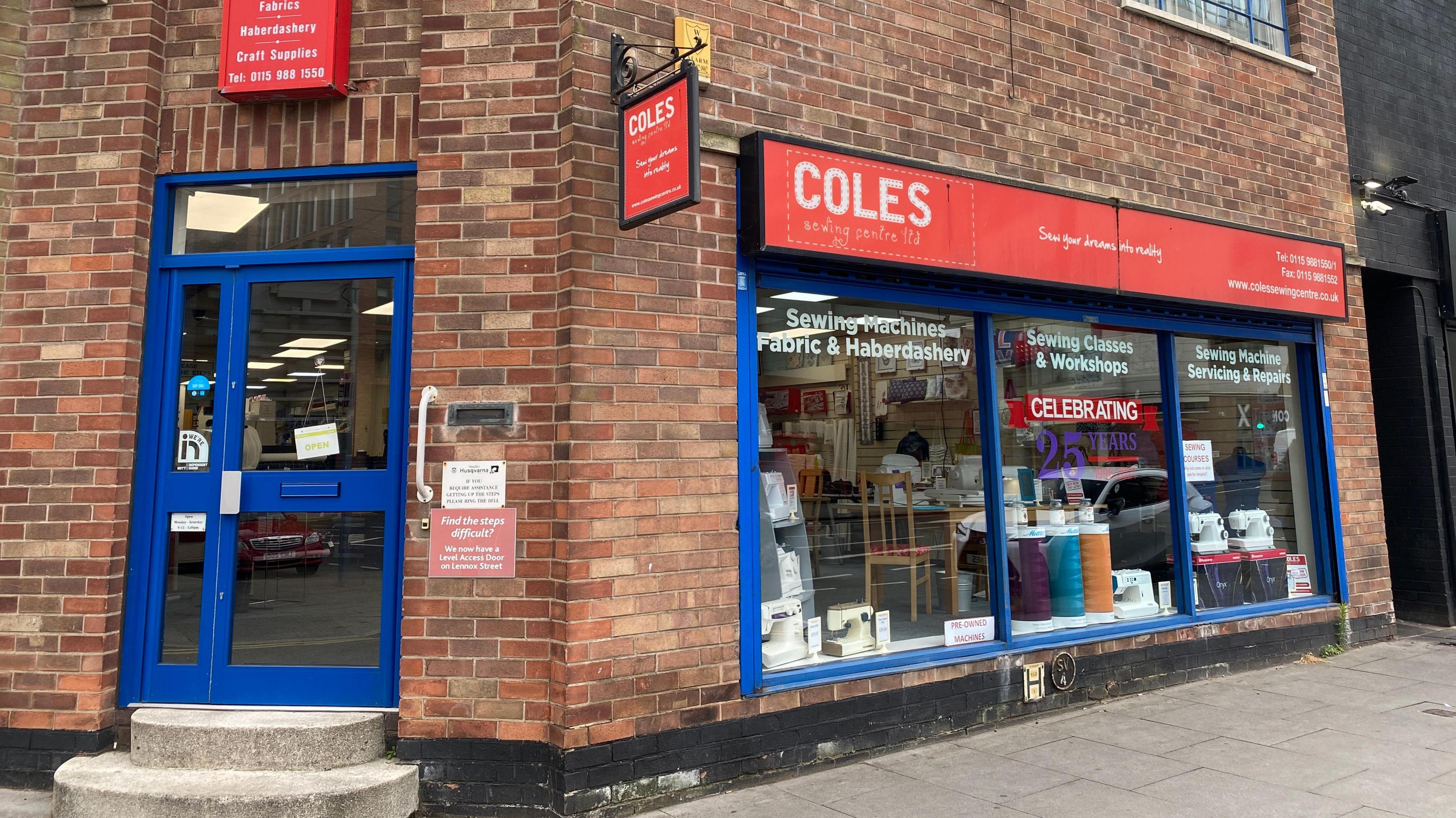 A red brick shopfront with two large blue windows and red signs for Coles Sewing Centre