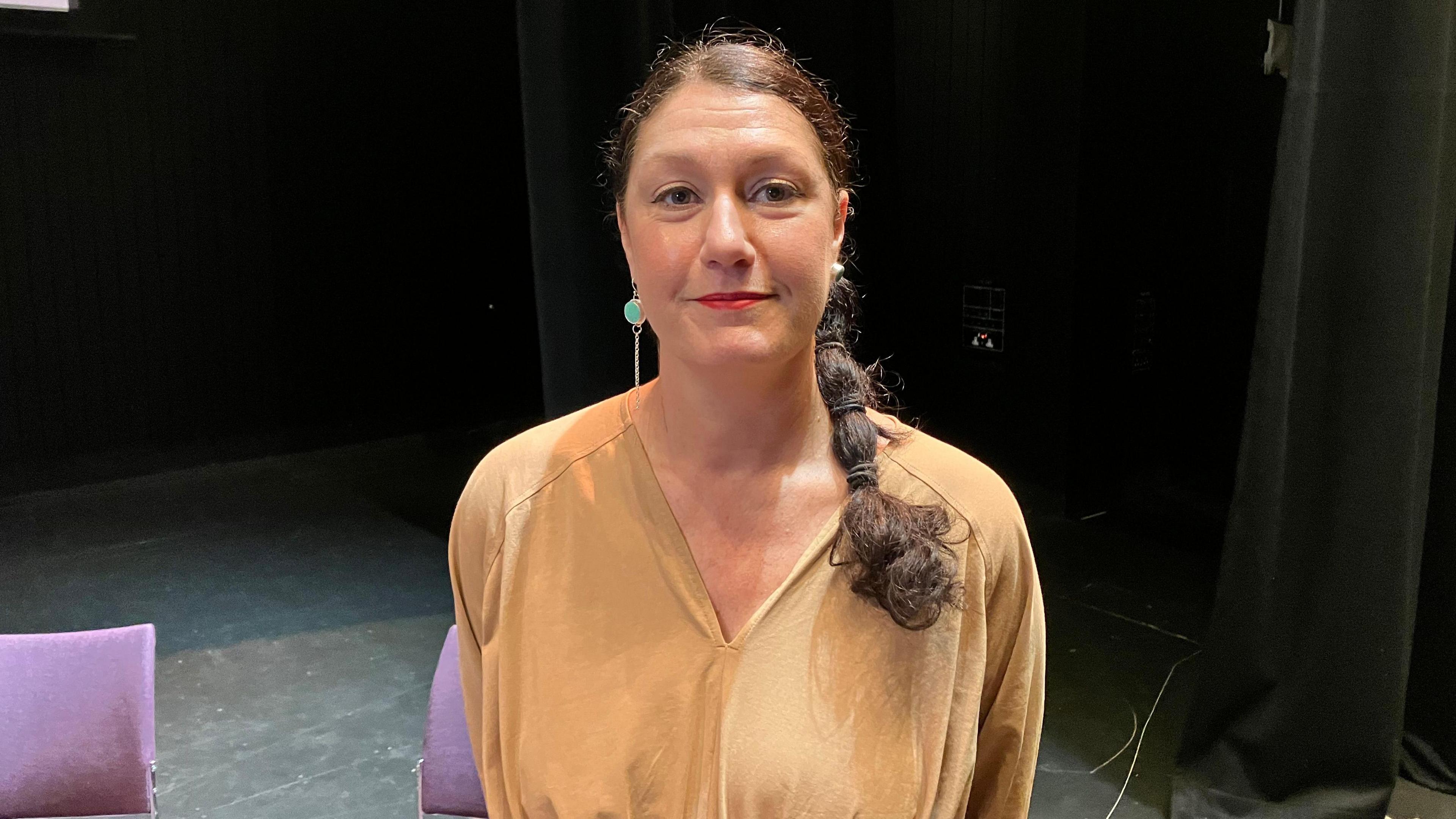 Natasha Almond, from Good Organisation, is looking straight at the camera. She has black hair in a plait and is standing on a stage at York St John University's lecture theatre.