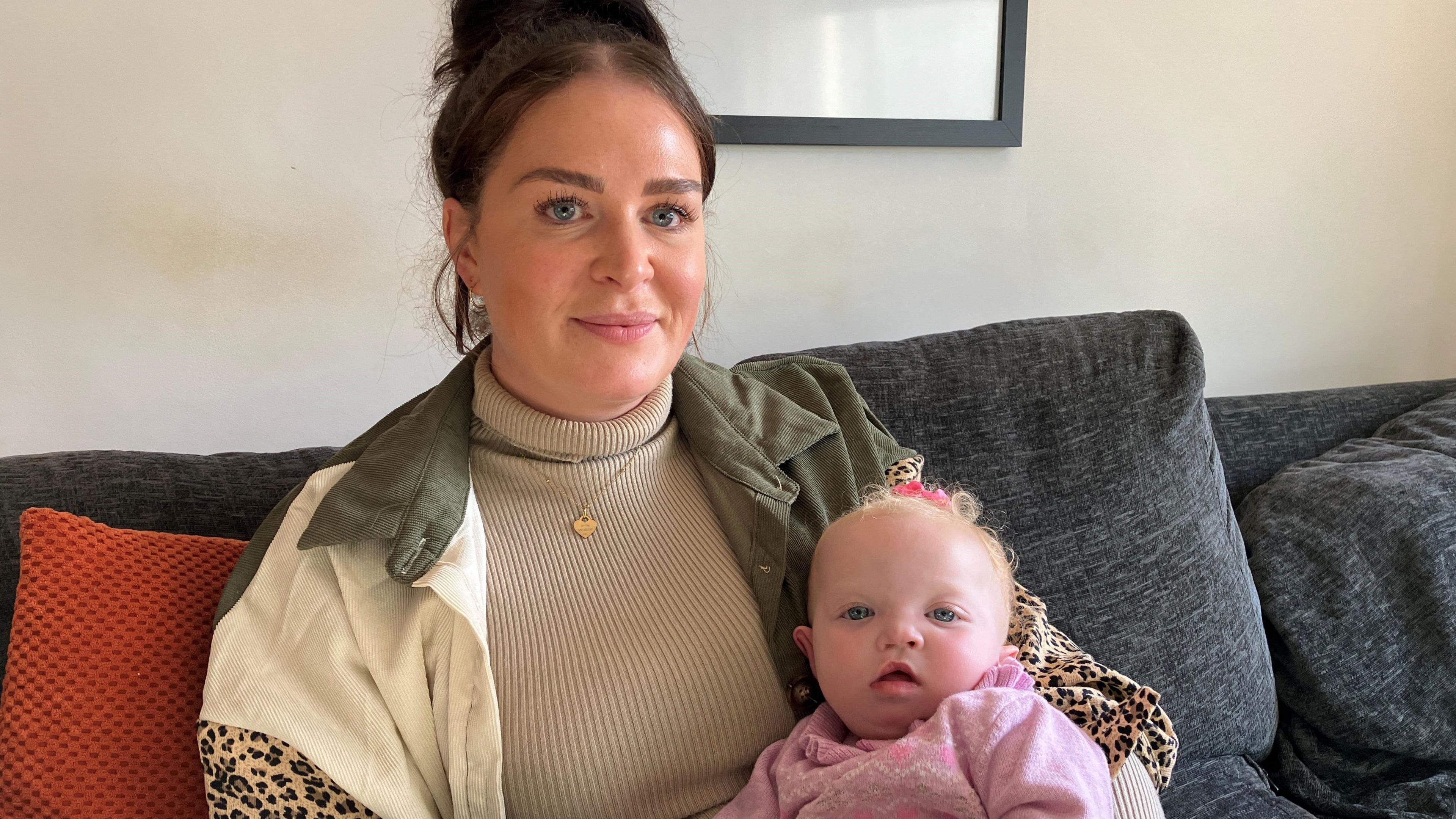 A woman and baby sat on a sofa looking at the camera