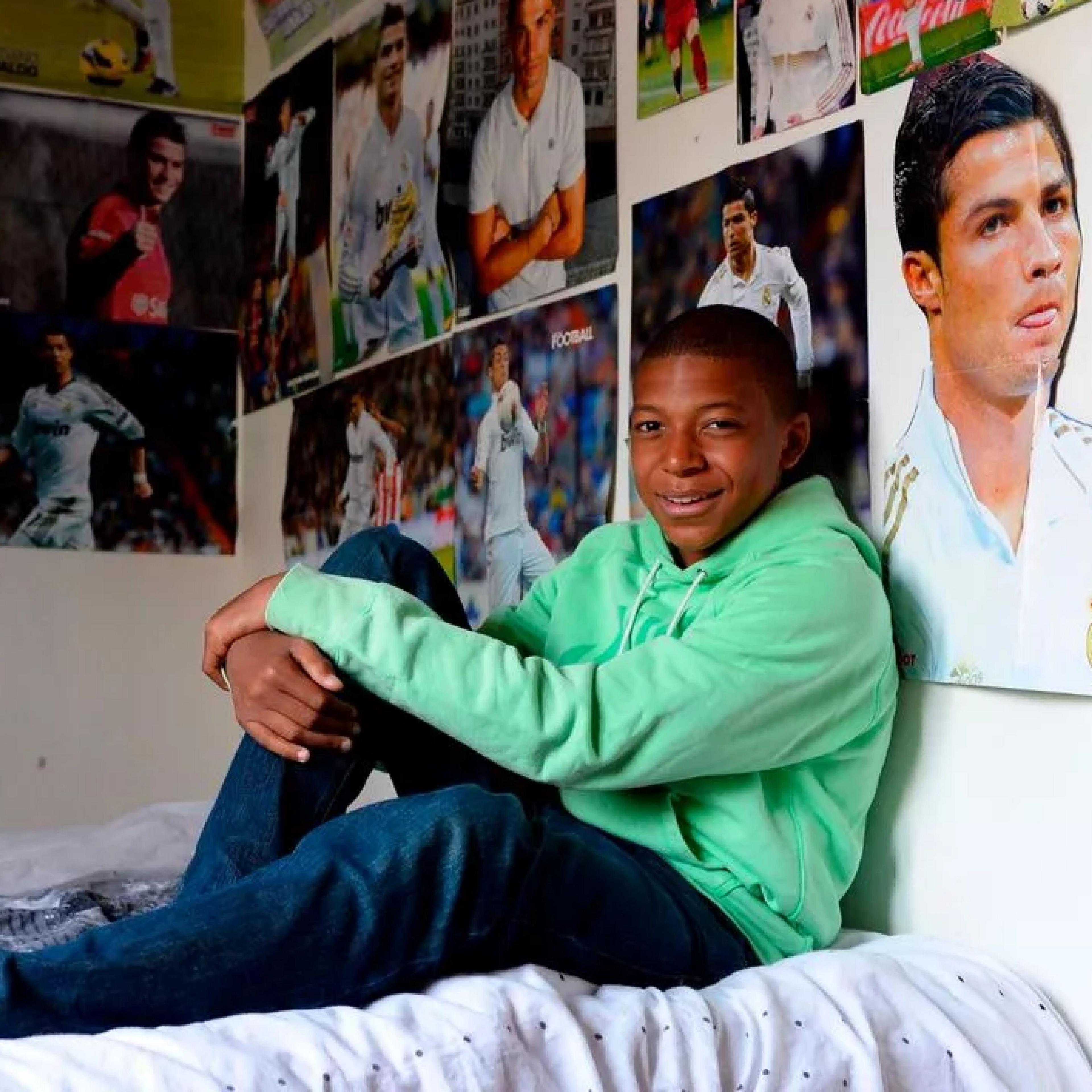 Kylian Mbappe sits on his bed with posters of Real Madrid's Cristiano Ronaldo all around him
