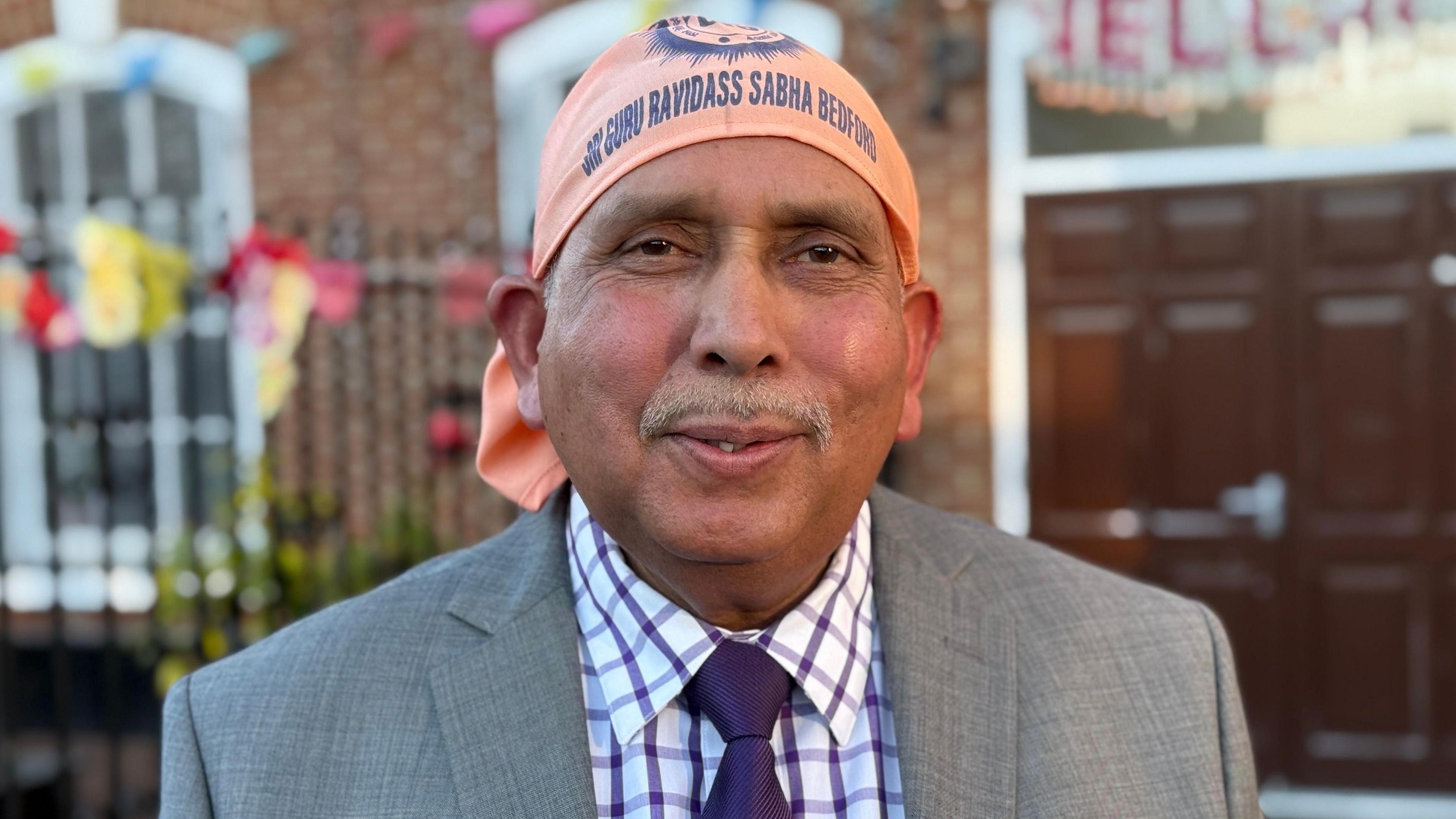 Jaswinder Kumar in a grey suit with a white and purple checked shirt. He is also wearing a purple tie and is looking and smiling at the camera. 