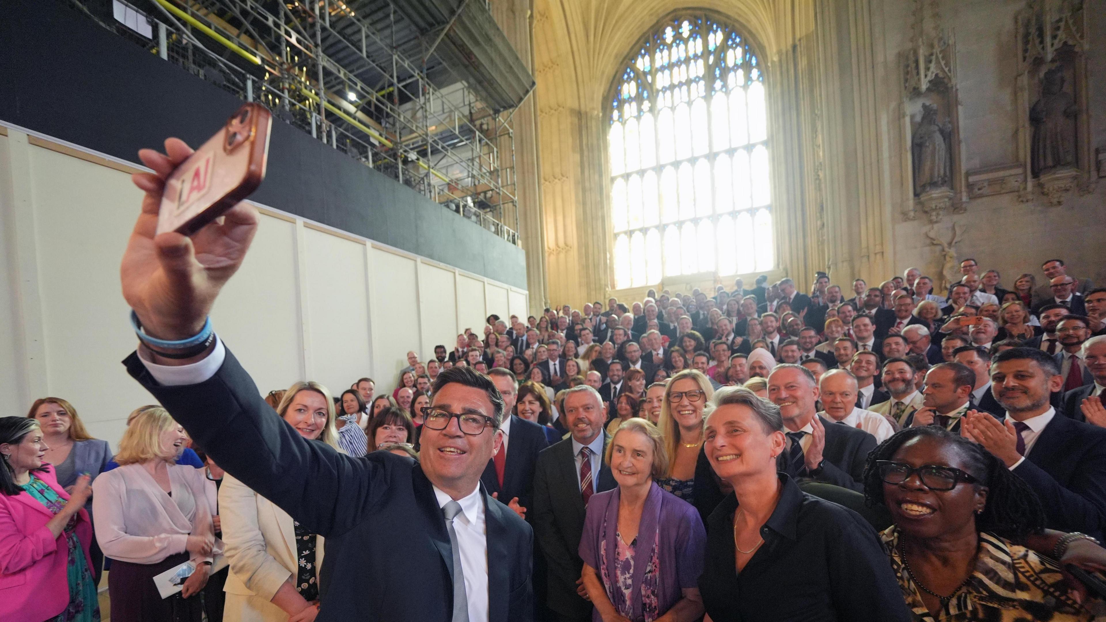 Andy Burnham in Westminster Hall with his arm raised up to take a selfie of himself and the group of around 200 Labour MPs standing behind him. The MPs standing immediately next to him include Nia Griffith, Kate Osborne and Paulette Hamilton
