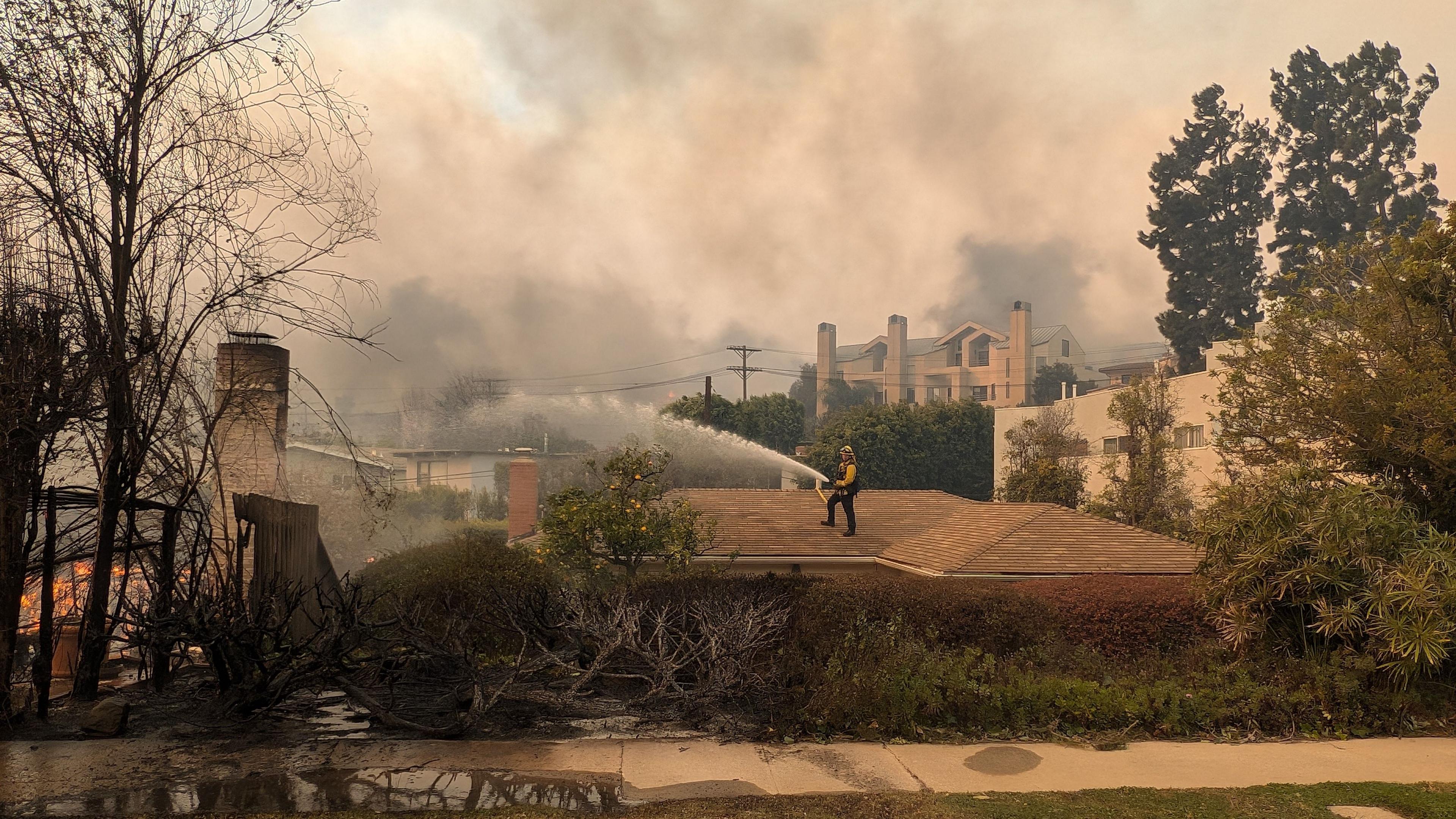 A fireman houses down a fire while standing on a roof