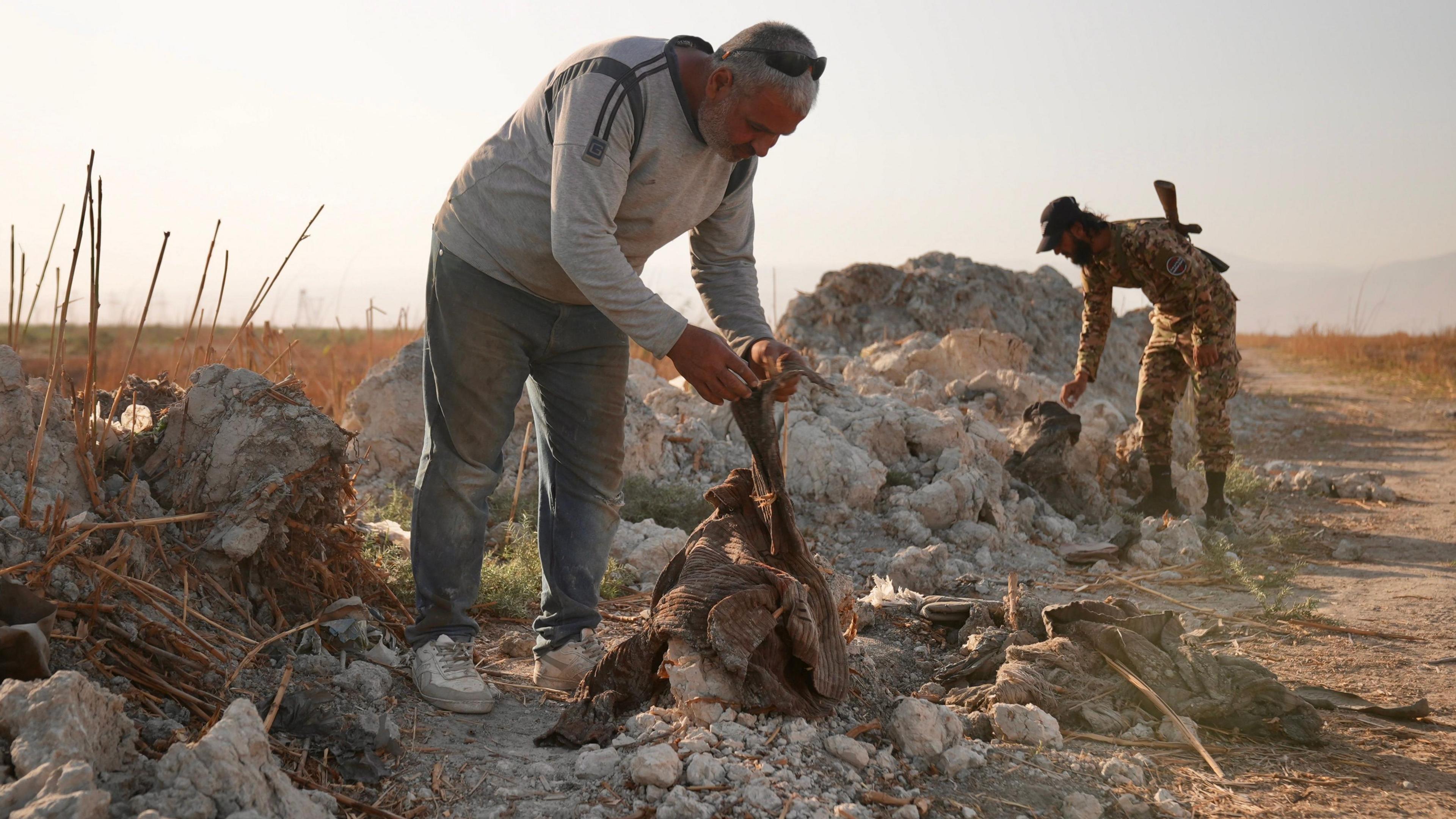 A man bends over a decaying item of clothing, looking at it.