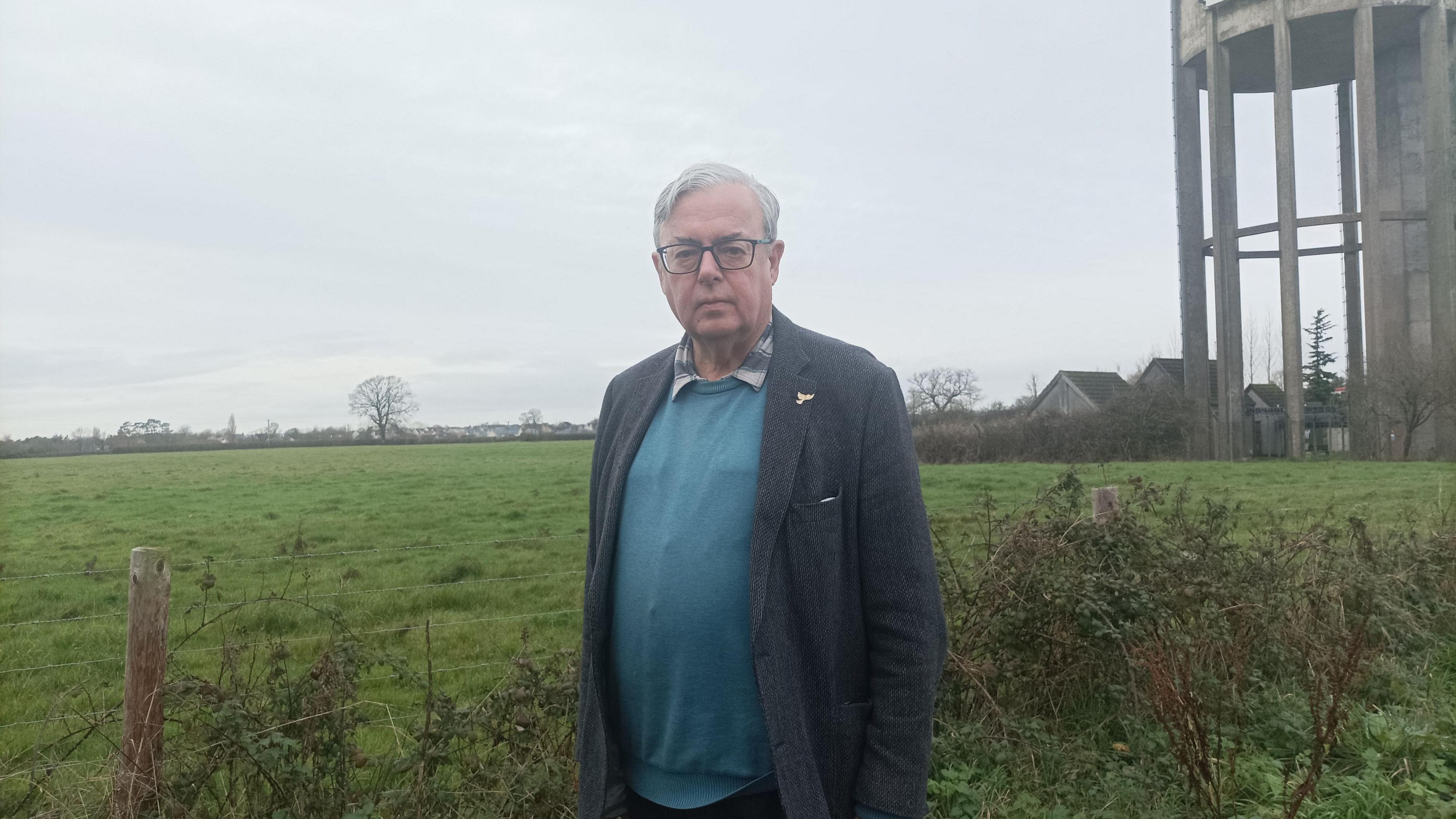 A man standing in front of field with water tower off to the right