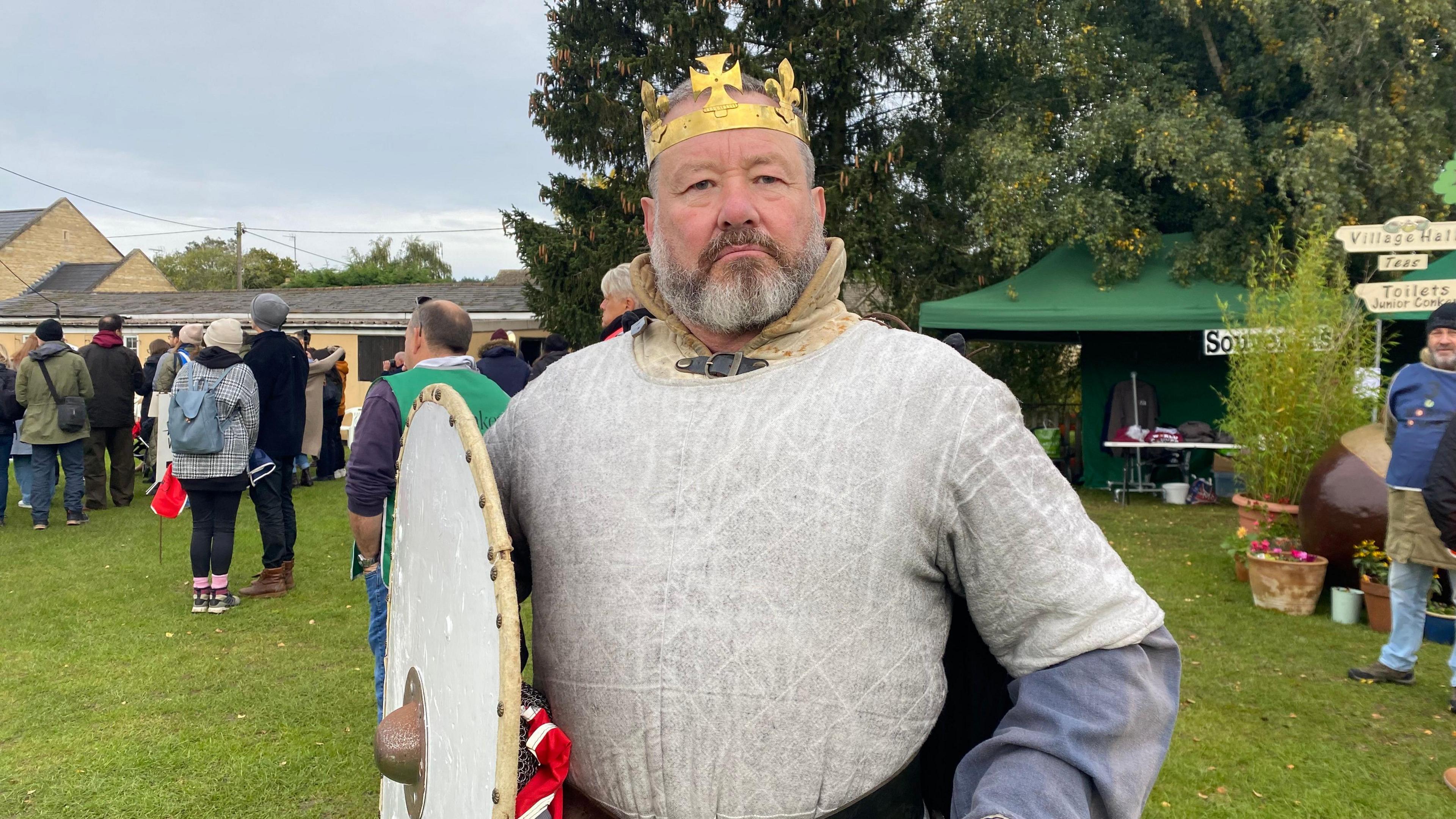 A man with a grey beard dressed in a gold crown and silver shirt holding a shield. He is William the Conkerer