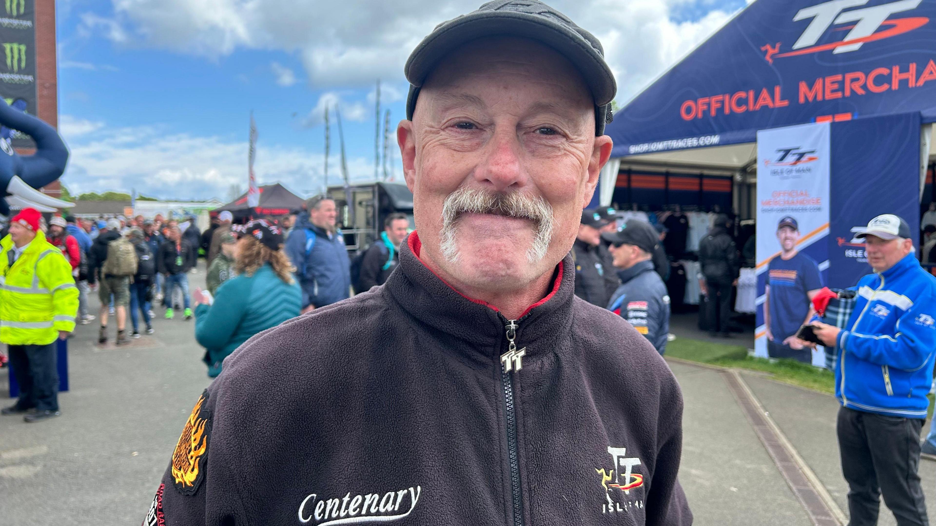 A man wearing a black jacket and cap at the TT Grandstand