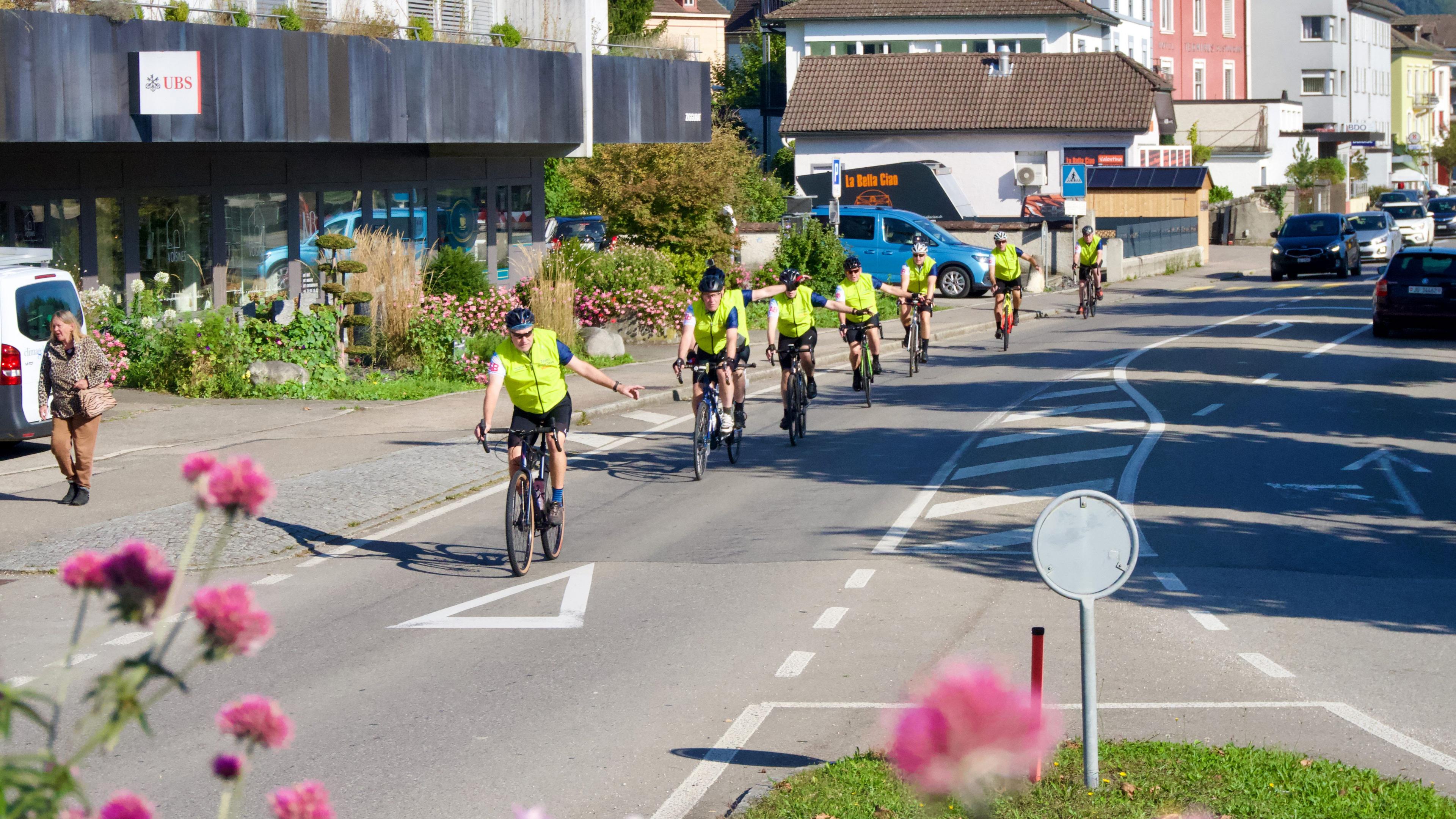 Eight cyclists on a road in the town centre approaching a roundabout