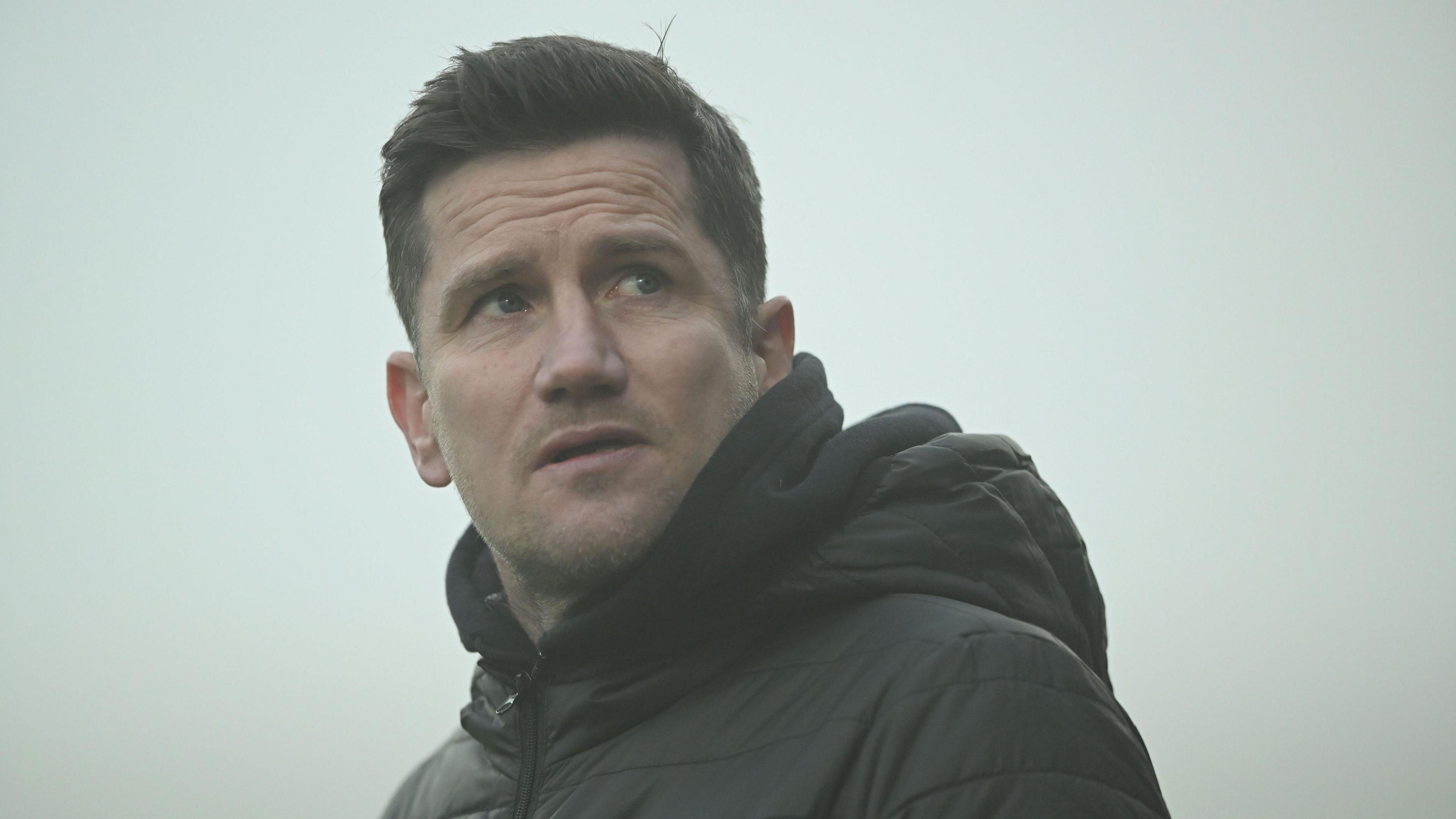 Crewe boss Lee Bell looks up into the stands from the touchline during a game