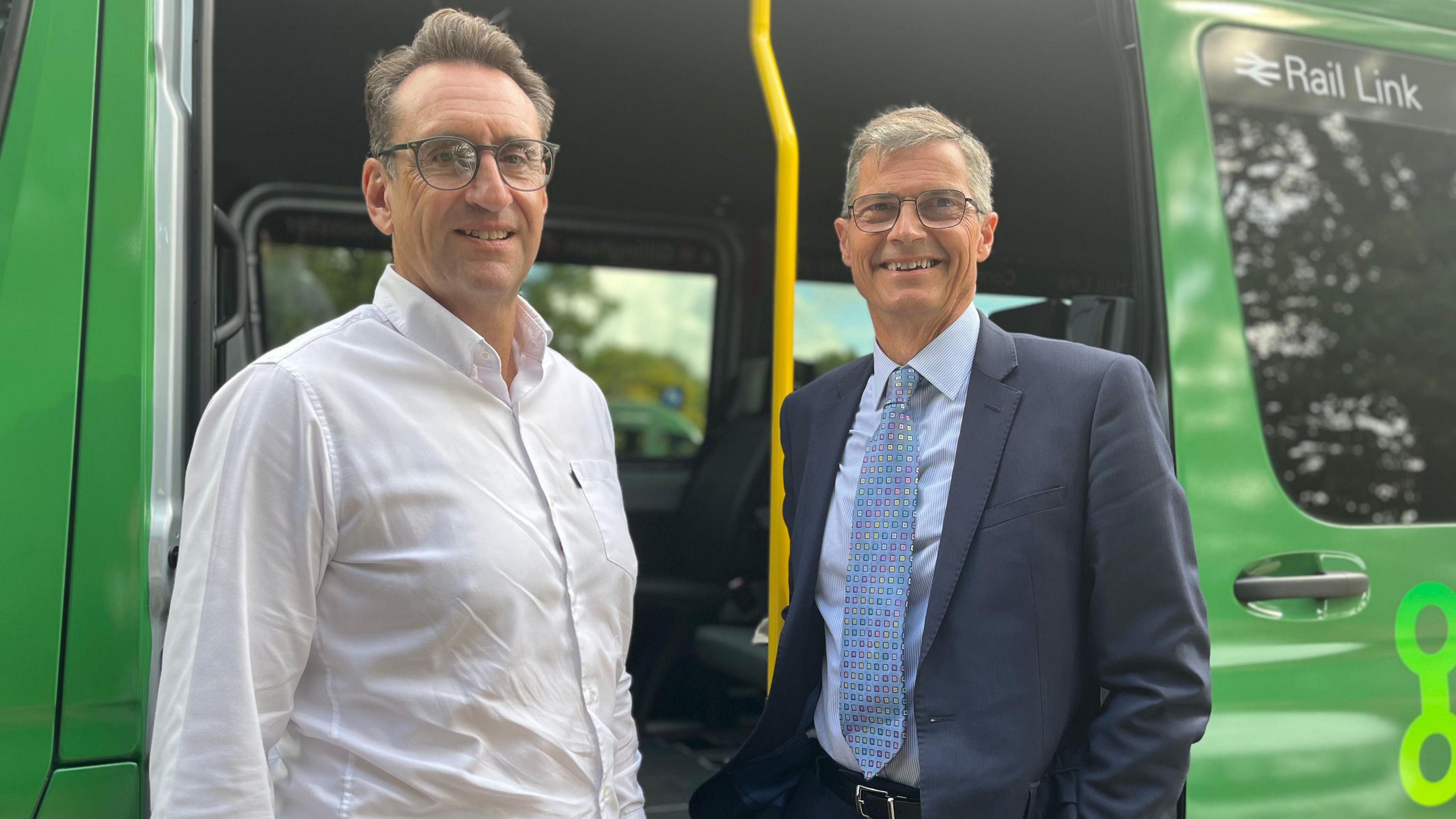 Jason Salter and councillor Martin Smith smile at the camera while standing in front of the open side door of a green minibus. Jason is wearing a white shirt and glasses and Martin is in a suit and tie.