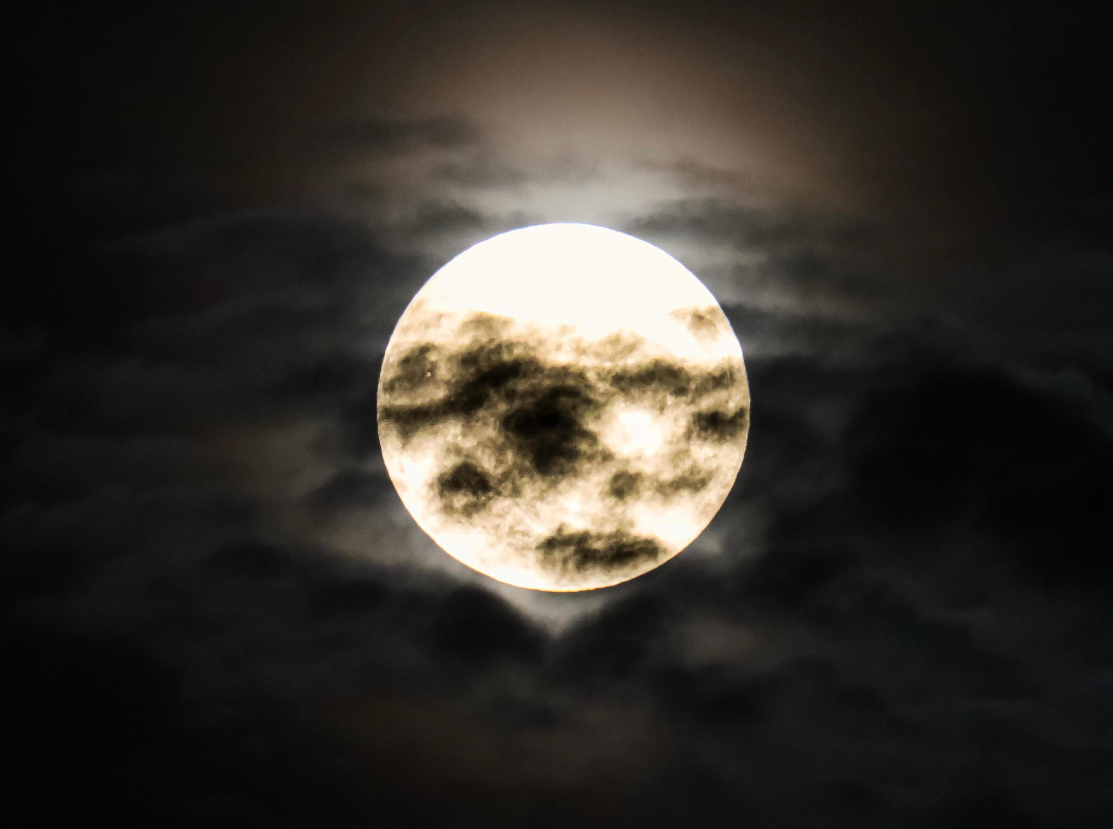 A large white Strawberry Moon in the night sky with black clouds crossing over it