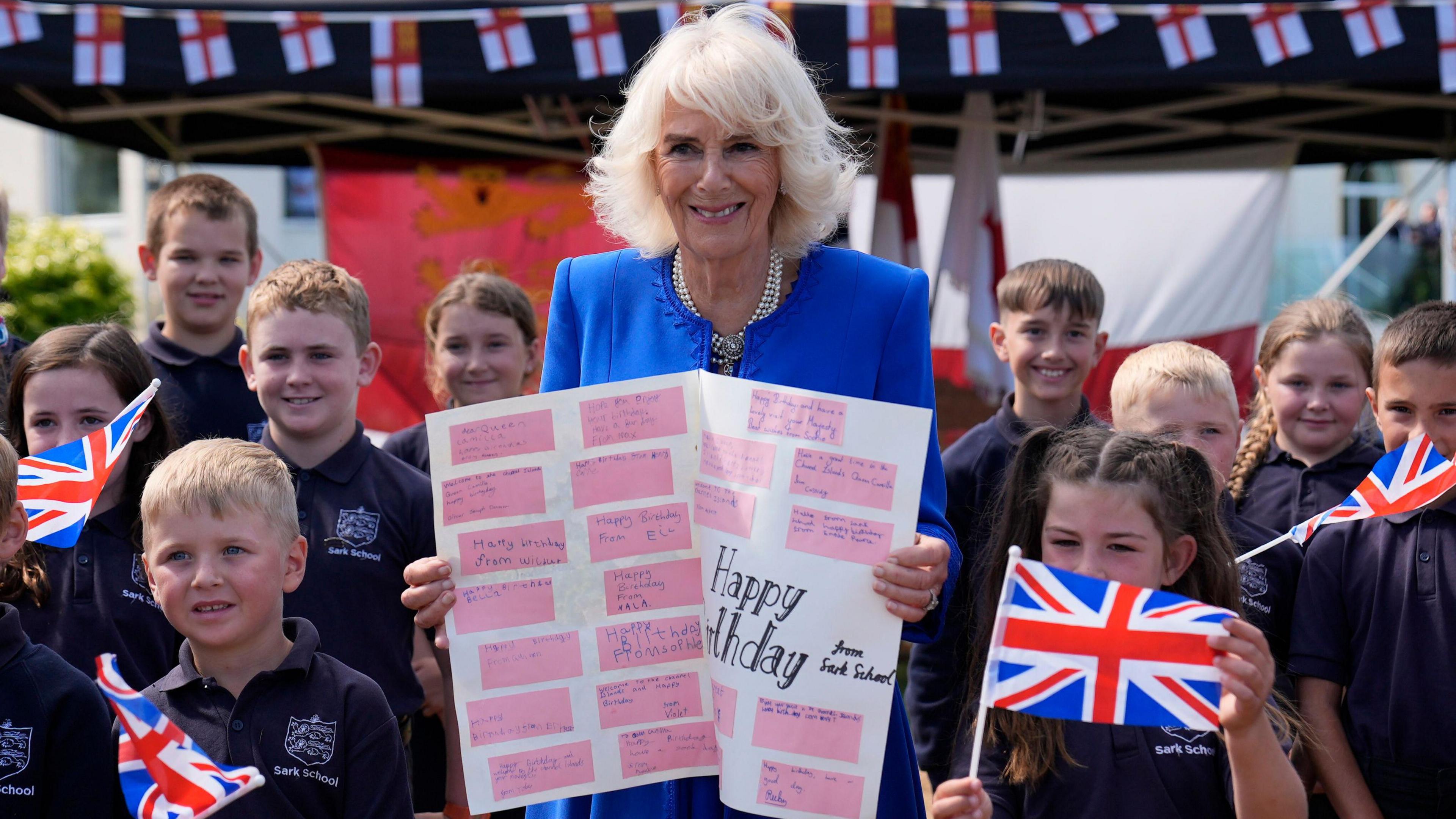 Queen Camilla poses with local school children holding a birthday card, during a visit to Les Cotils at L'Hyvreuse, in Saint Peter Port, Guernsey