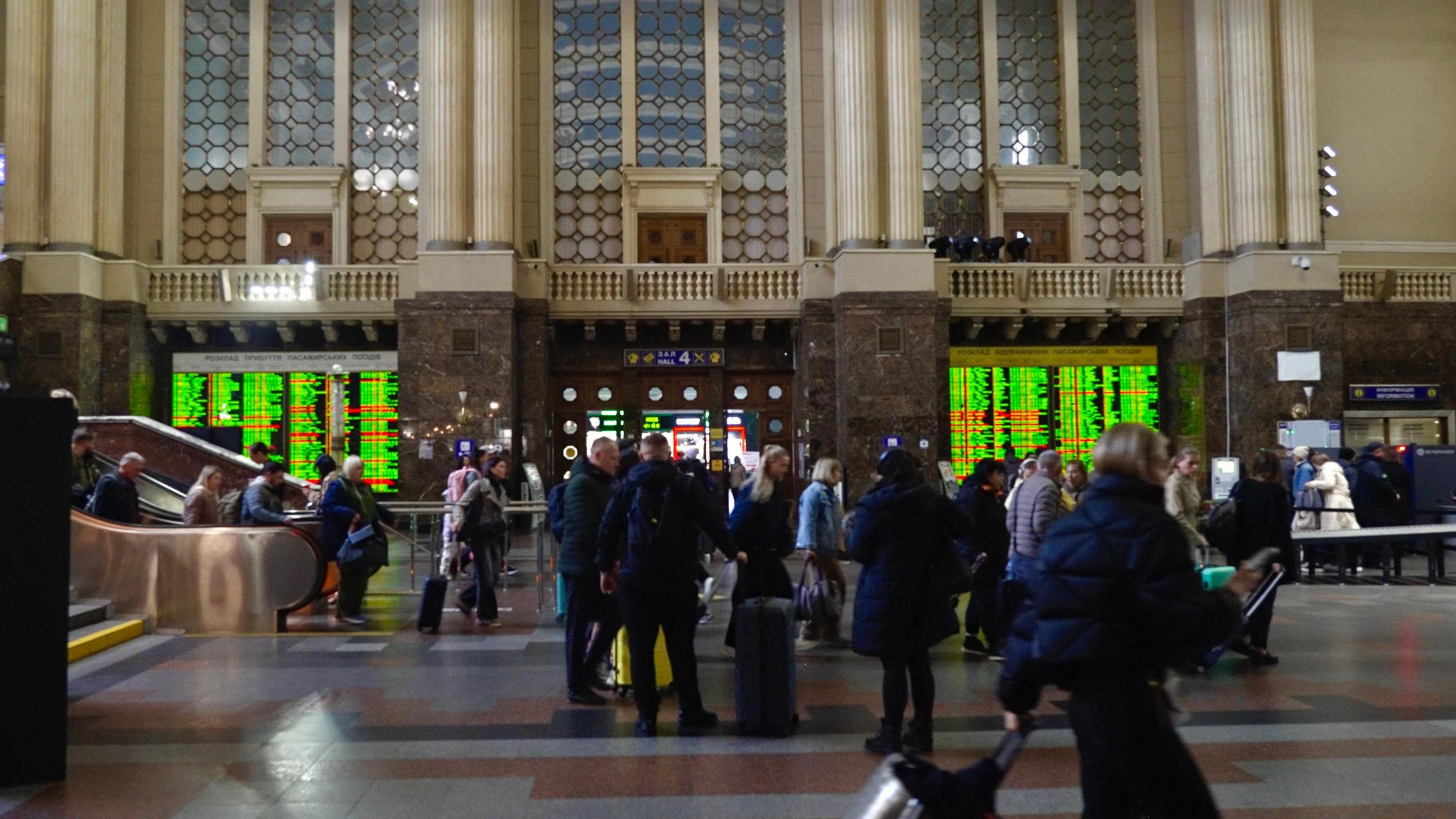 People rush through Kyiv central station, in front of large departure boards announcing the trains leaving in green text