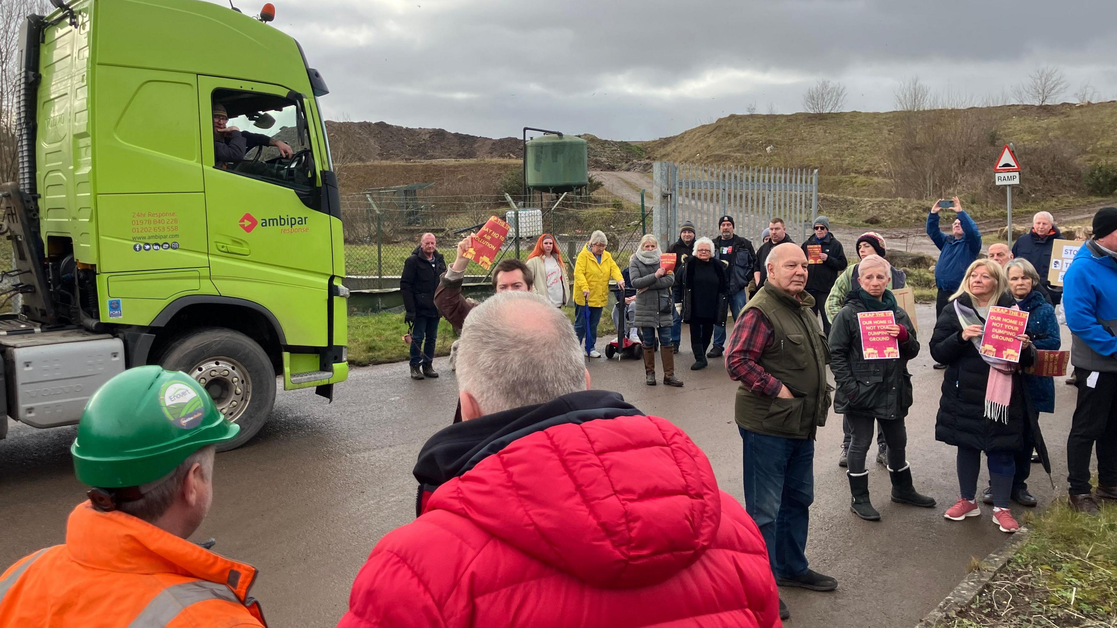 A group of people gathered outside the landfill entrance holding signs