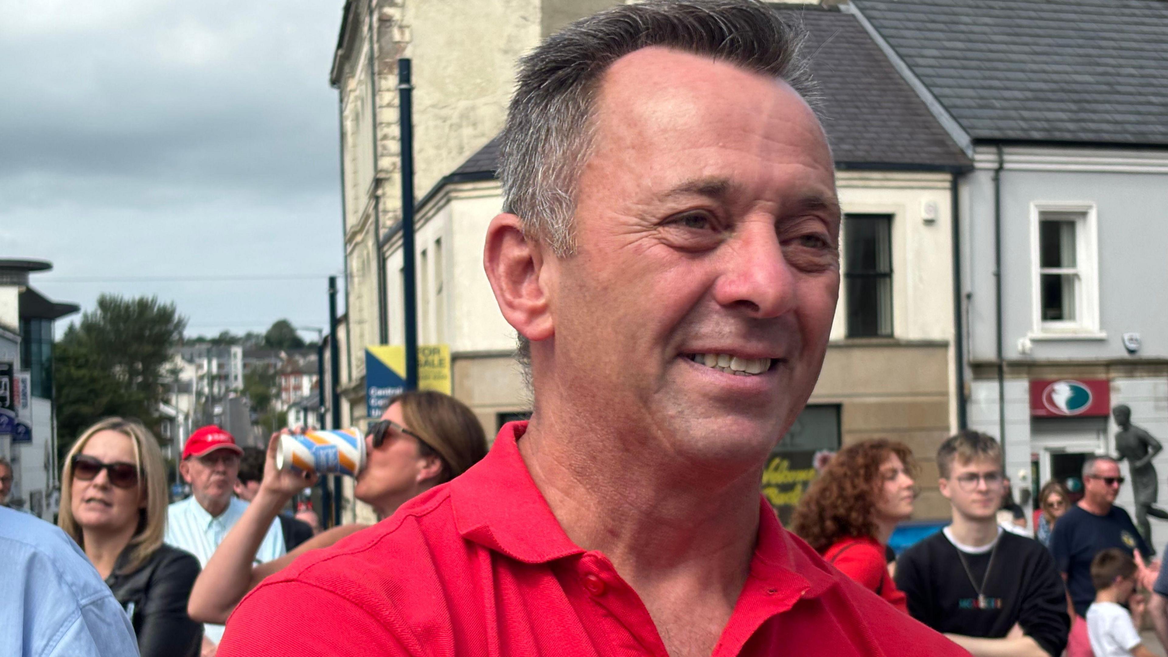 Man in a red t-shirt smiling with a crowd in the background