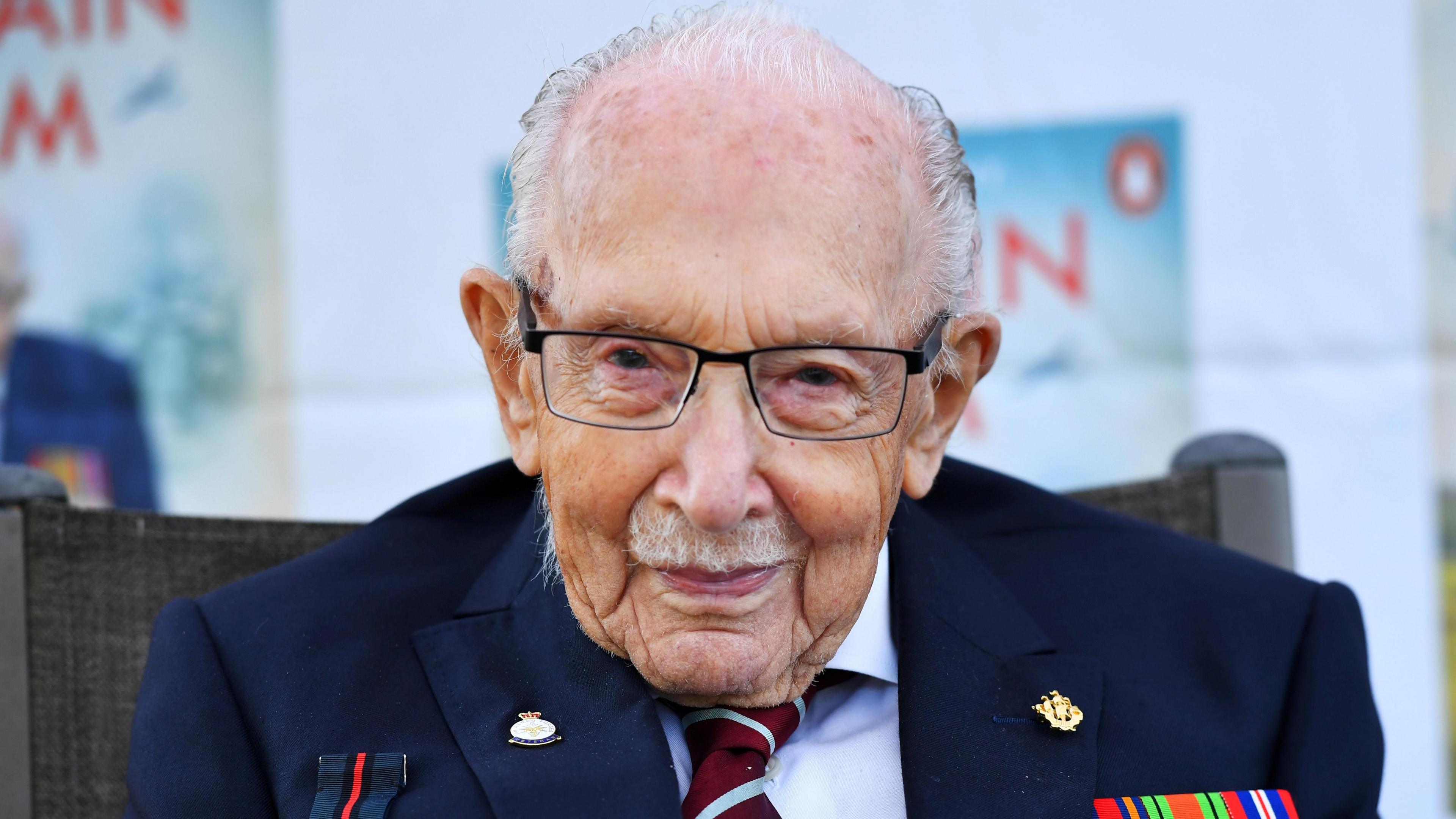 Captain Sir Tom Moore smiles at the camera as he launches his autobiography book "Tomorrow Will be a Good Day" at his home in Bedfordshire. Large versions of the book cover are behind him