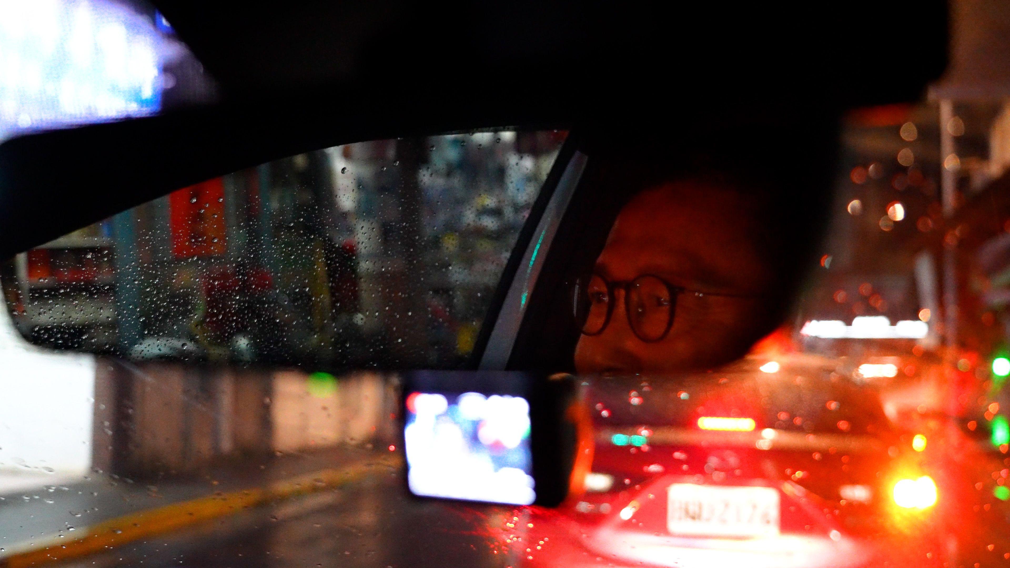 Chan's bespectacled eyes are visible in the mirror of the car as he drives in Taipei