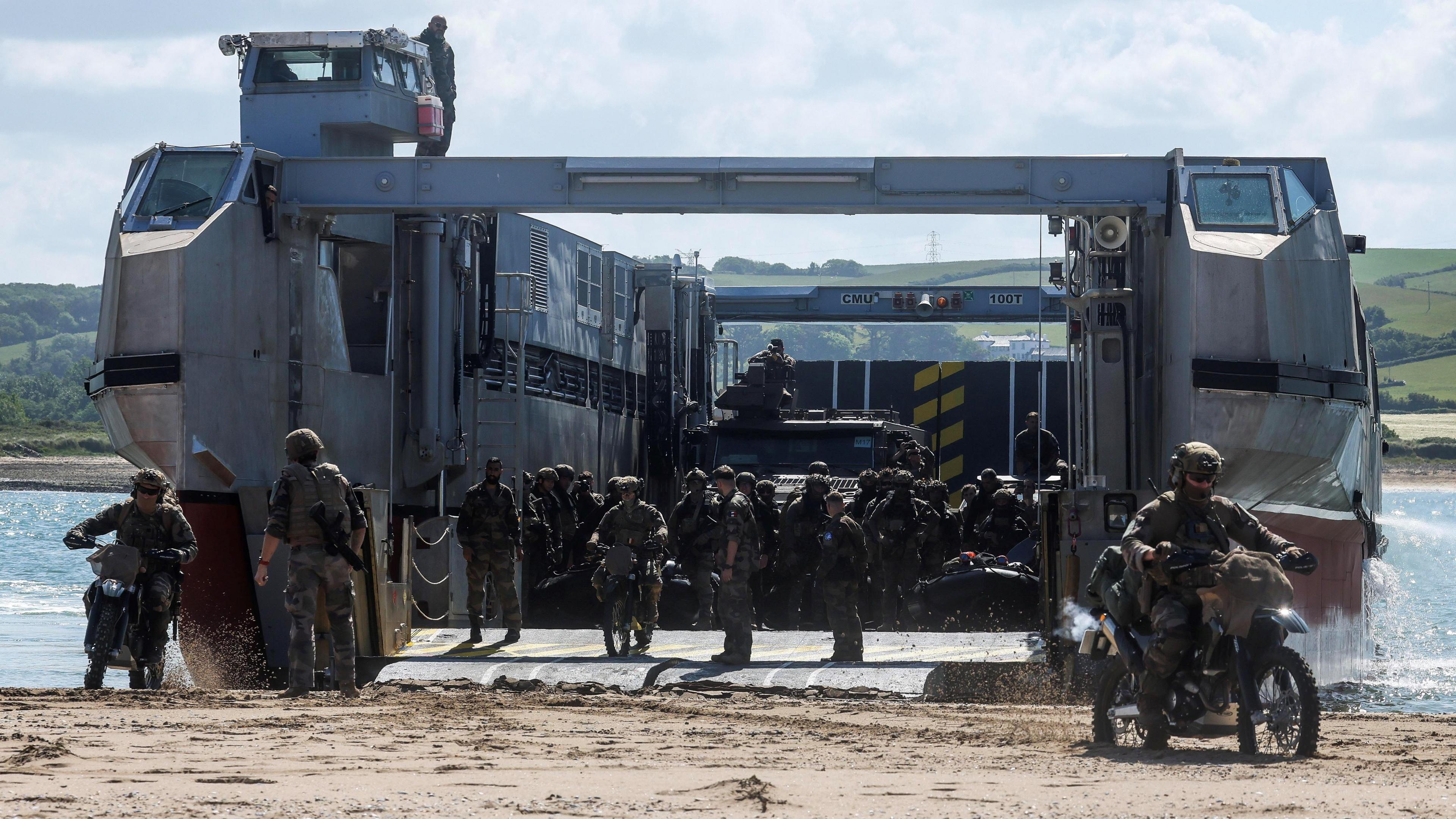 Troops and vehicles moving off a large landing craft on a beach