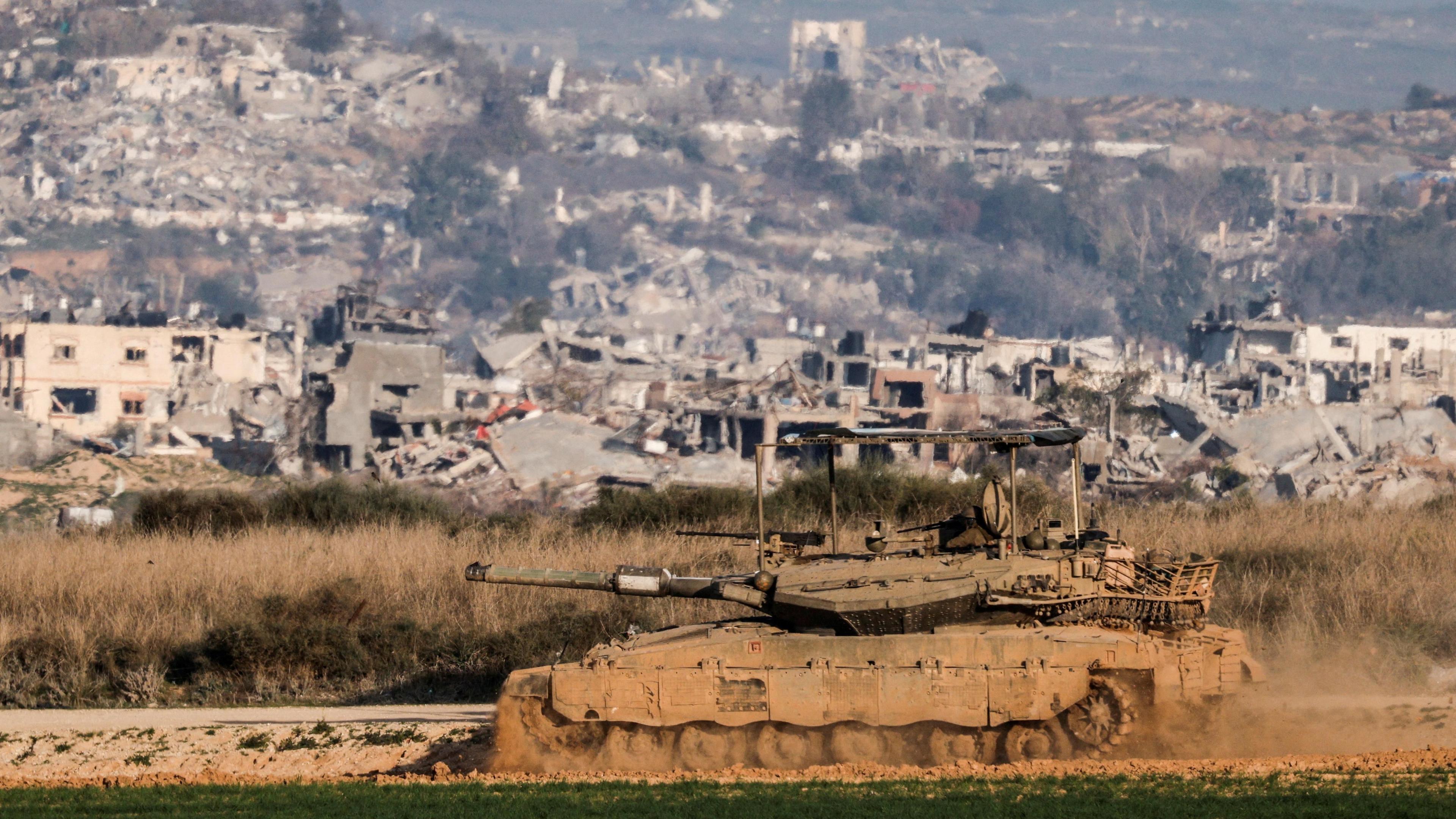 An Israeli tank manoeuvres near the Israel-Gaza border, with destroyed buildings inside Gaza visible in the background (19 January 2025)