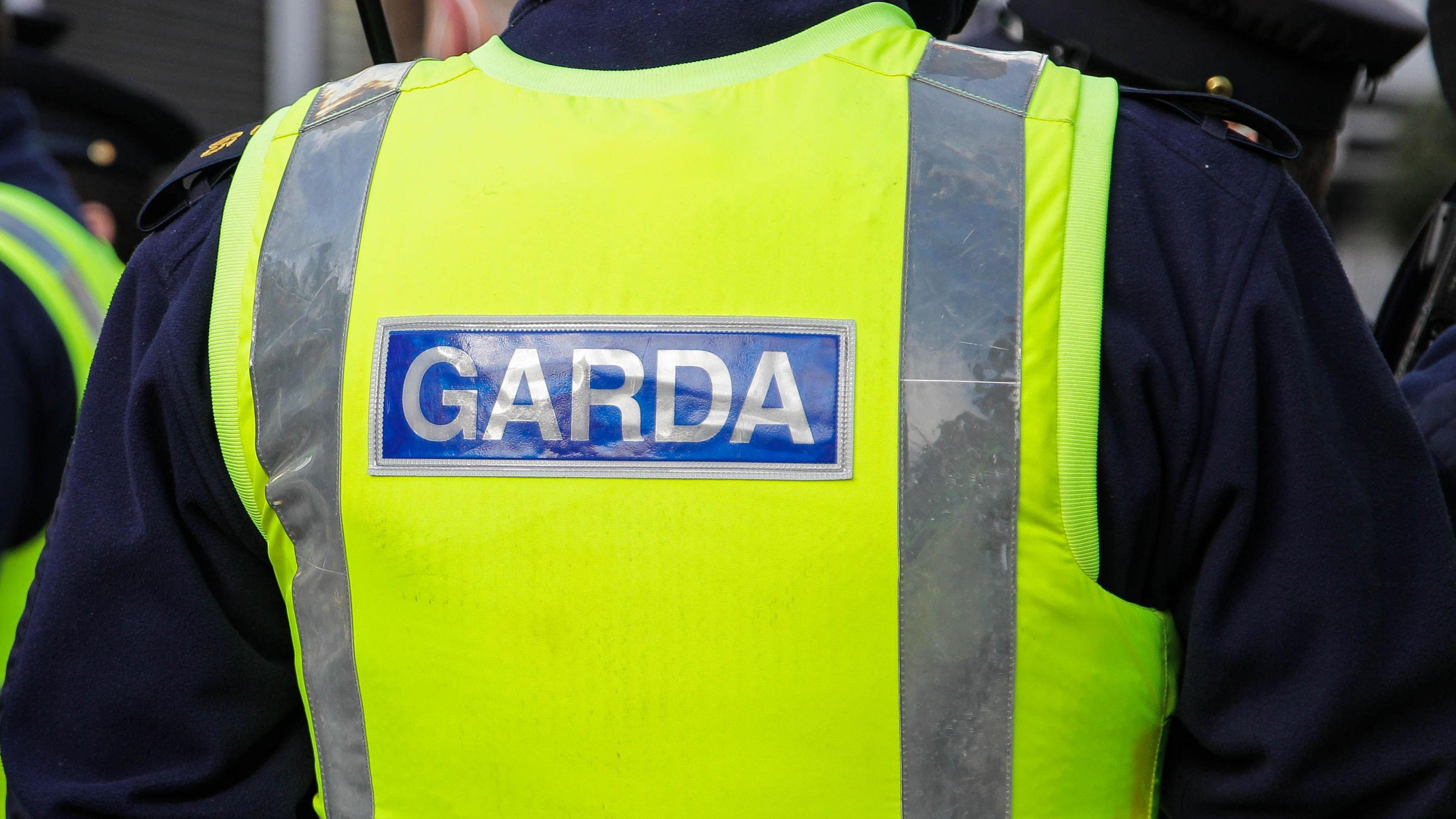 A yellow illuminous vest has the words 'Garda' on it in silver font with a blue background.