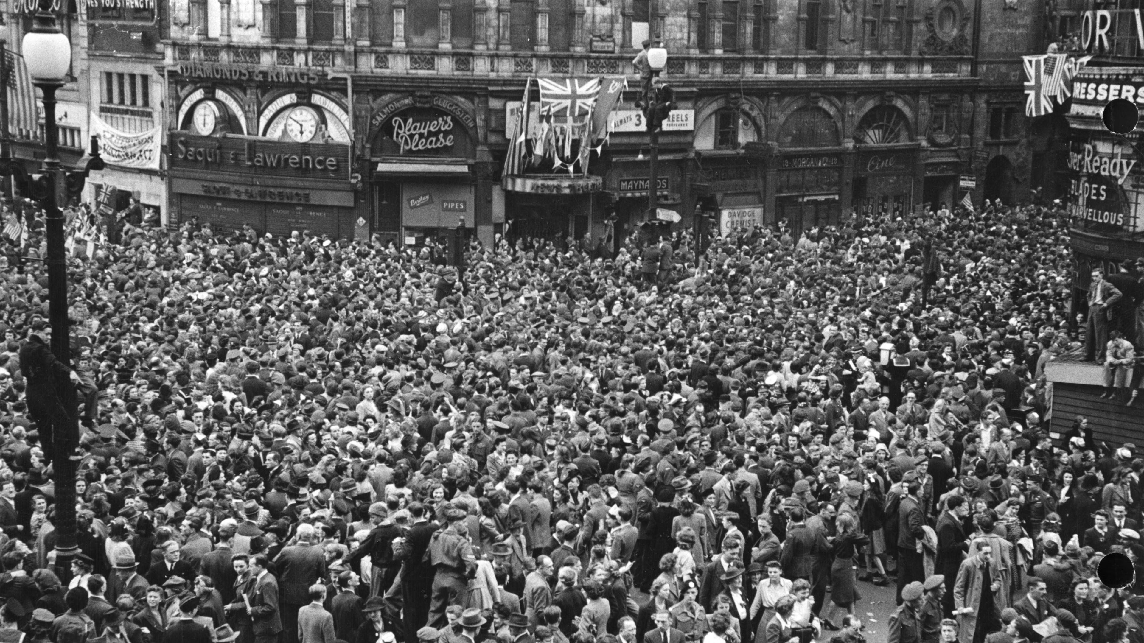 Black and white photo showing hundreds of people in central London celebrating VE Day.