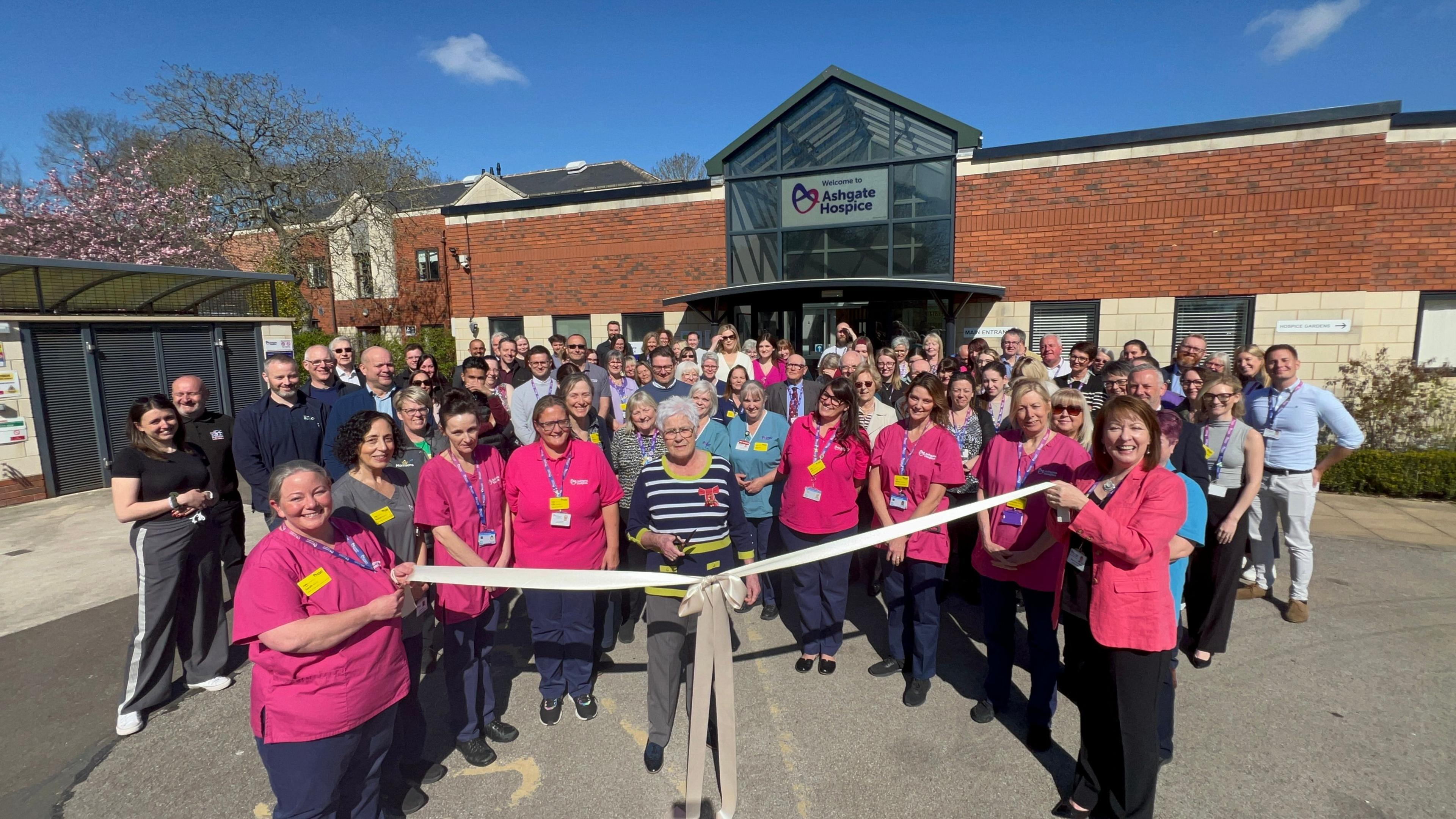 A large group of people with a ribbon being cut