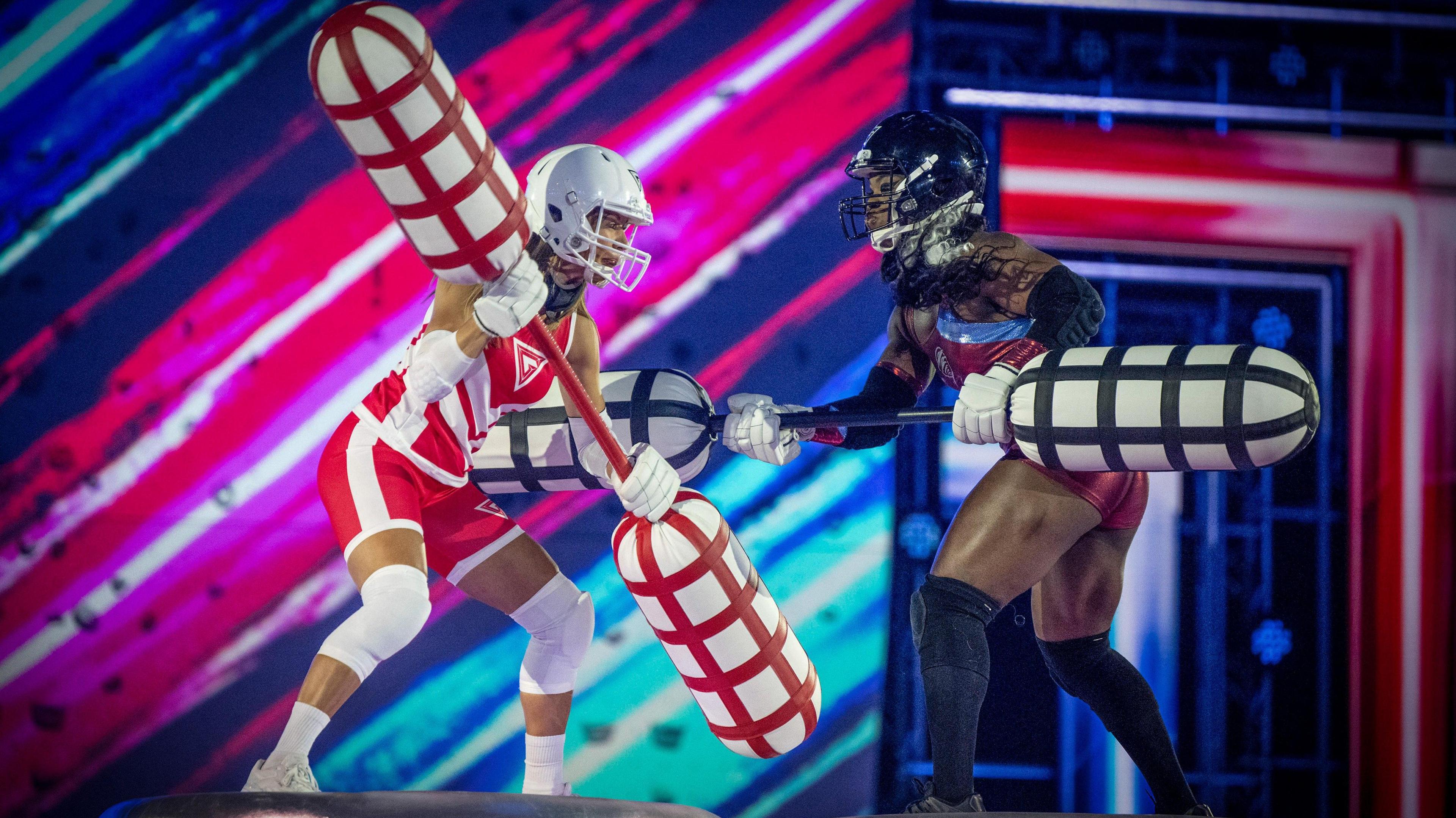 Two people holding giant sticks with foam ends, one person is wearing a red and white outfit, the other a red and blue outfit