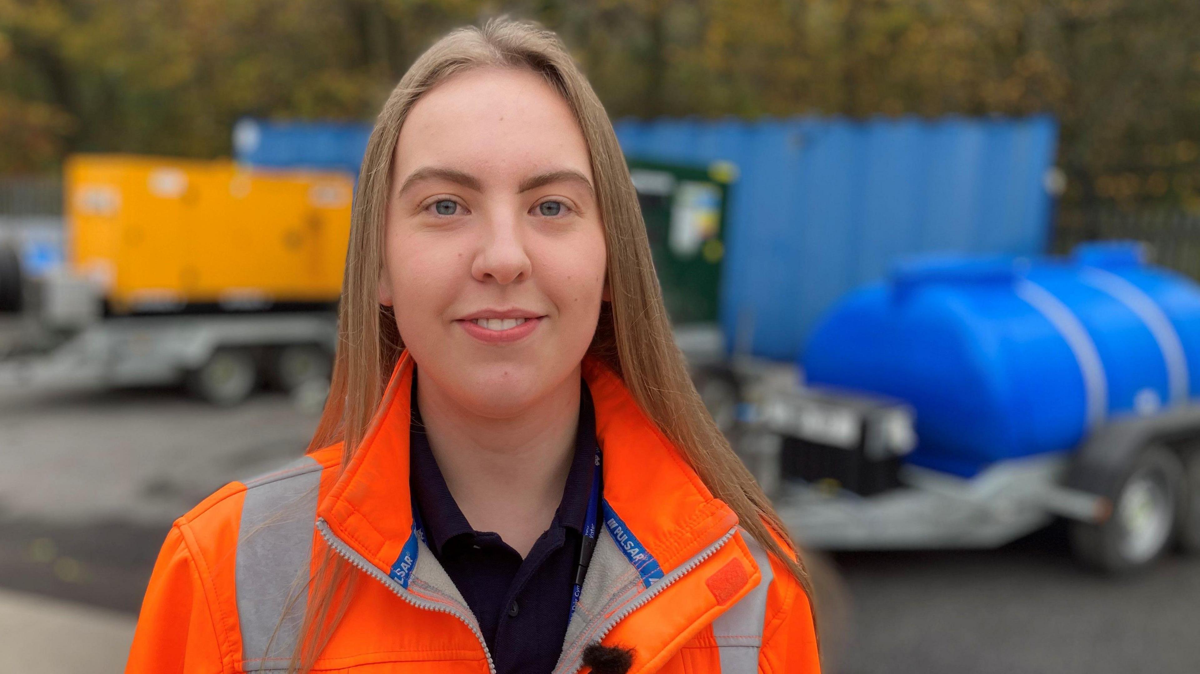 Lauren Johns, operational supervisor at Welsh Water's Clydach depot stands in front of water tankers in an orange hi-vis coat.