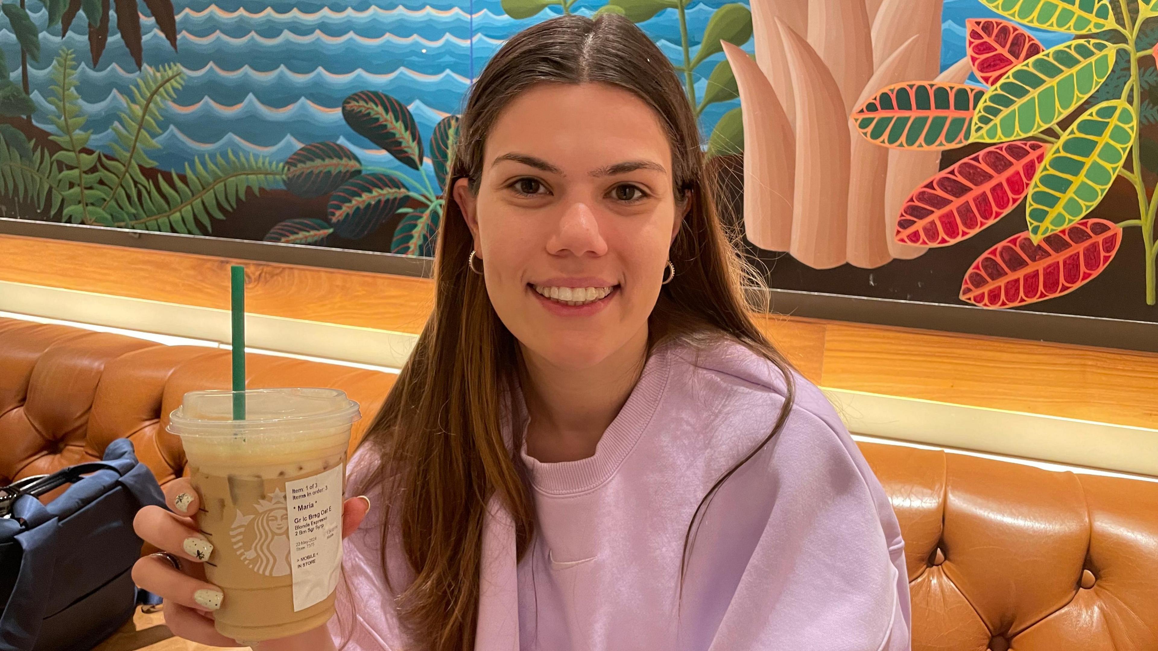 Maria Soare in a Starbucks cafe holds up an iced drink