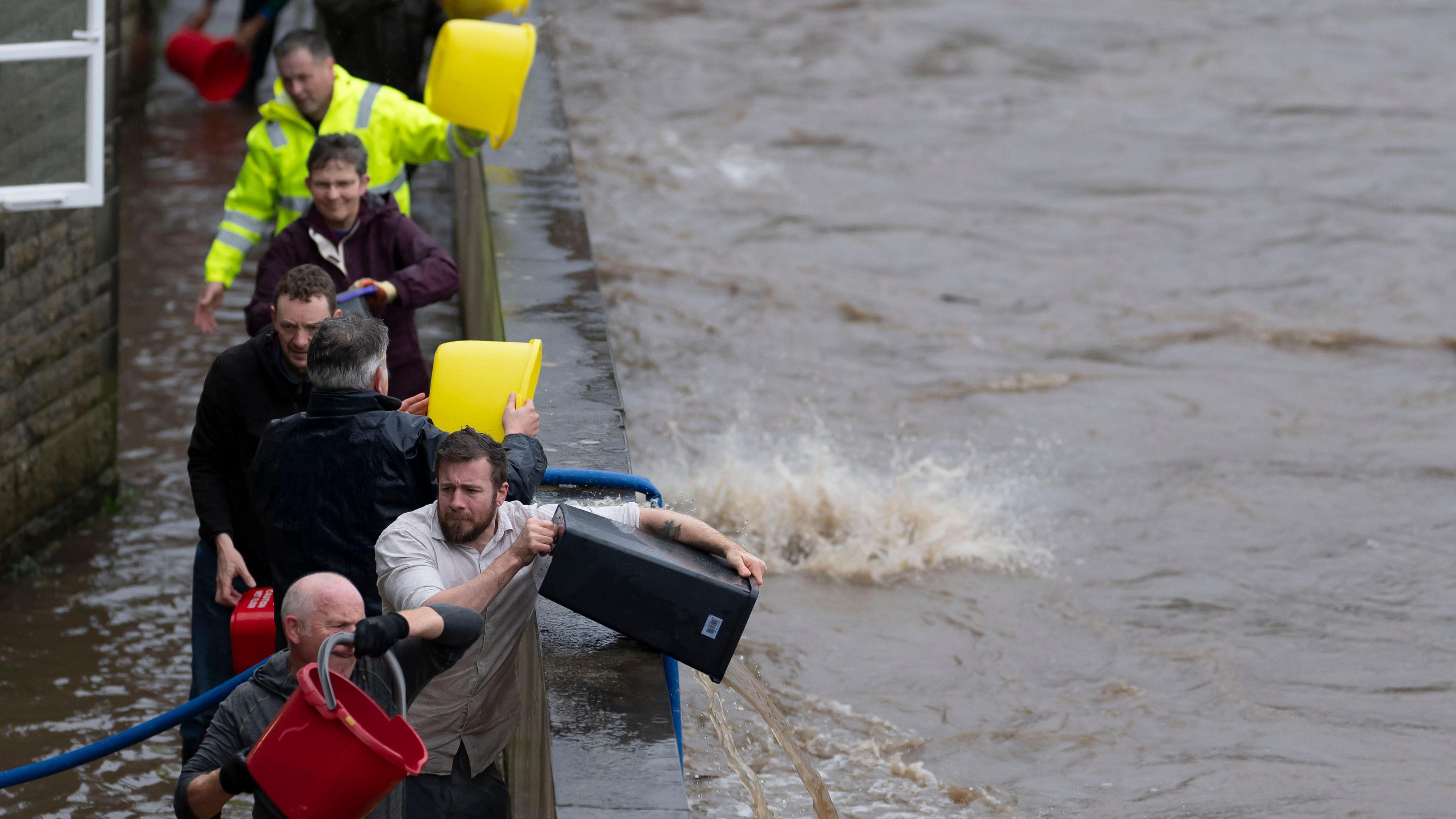 A line of men empty buckets of floodwater over a wall and into a river in Pontypridd
