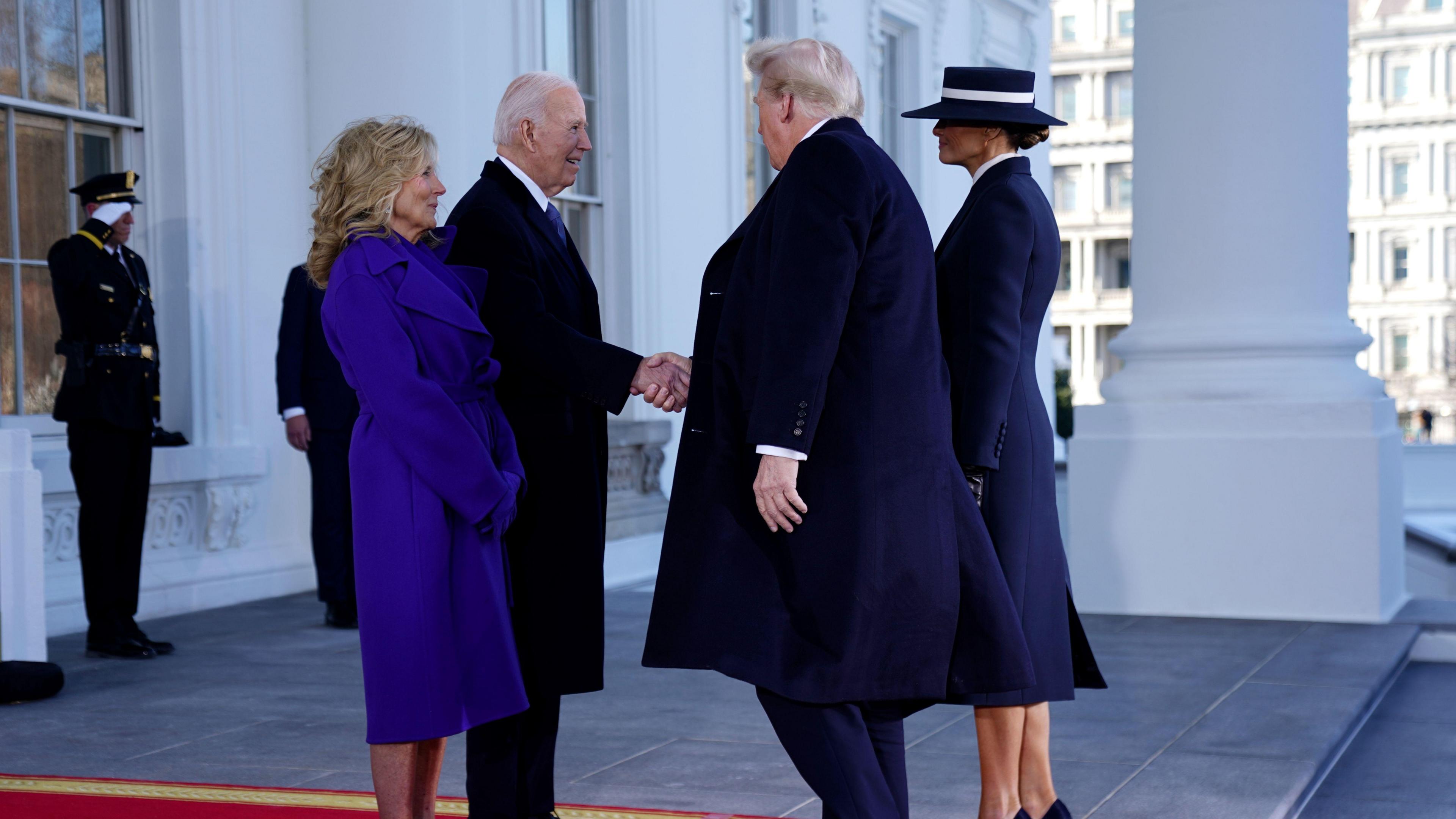 jill and jo biden standing opposite melania and donald trump on the steps of the white house with guards behind in salute