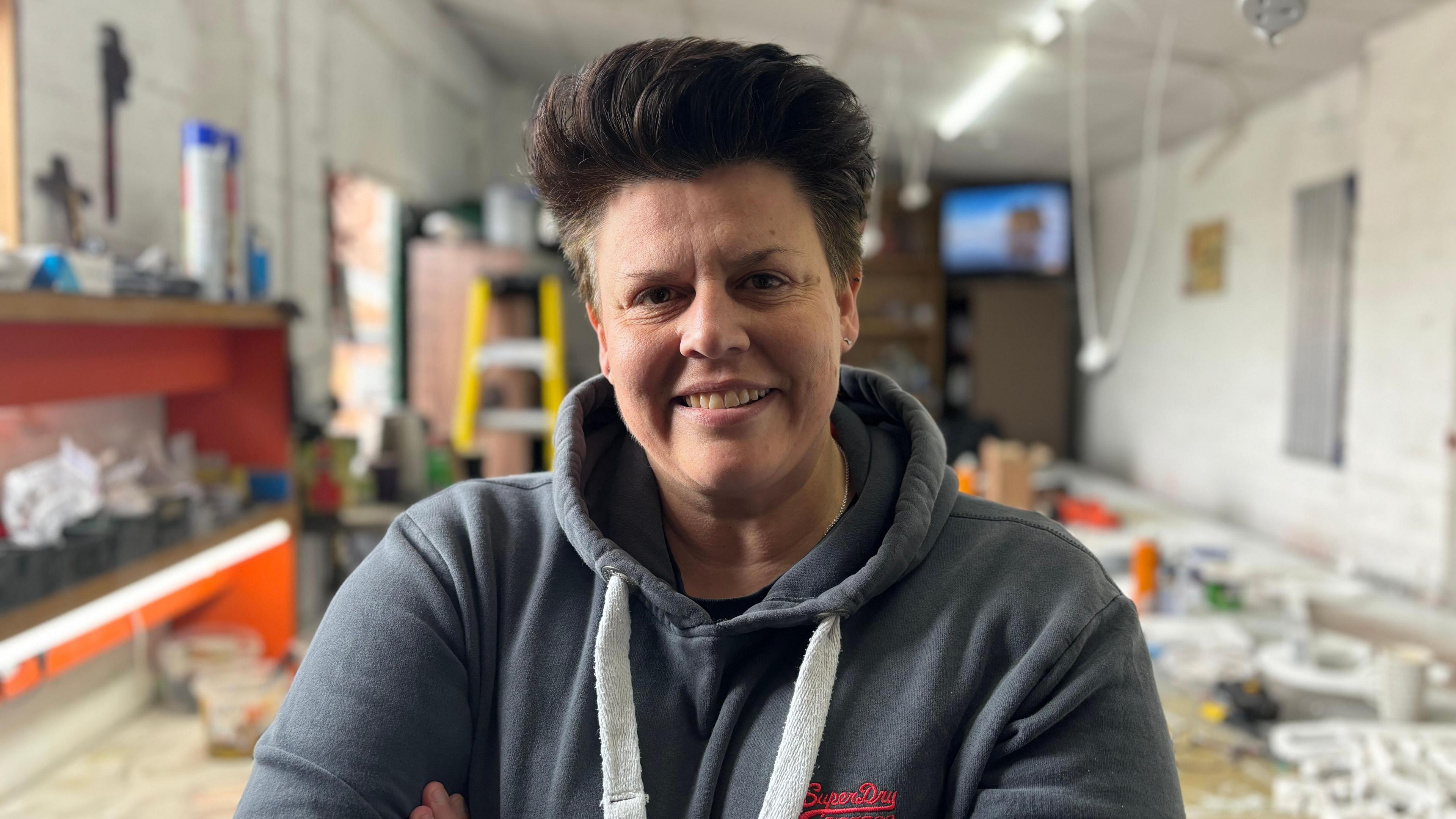 Sign maker Nichol Dexter, pictured in her workshop with short hair, wearing a hoodie