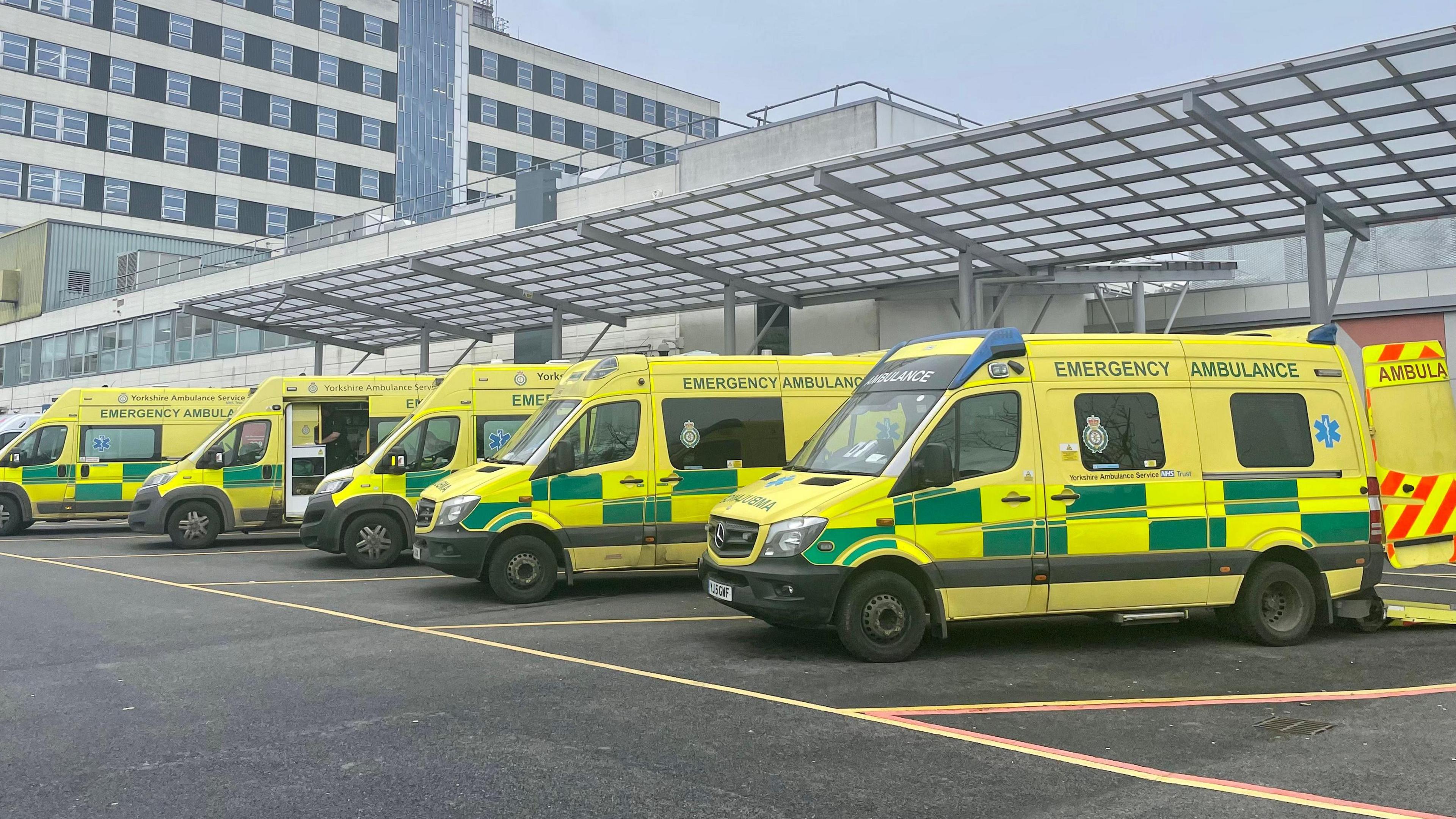 A row of ambulances are parked outside a hospital, ready to be dispatched for patients