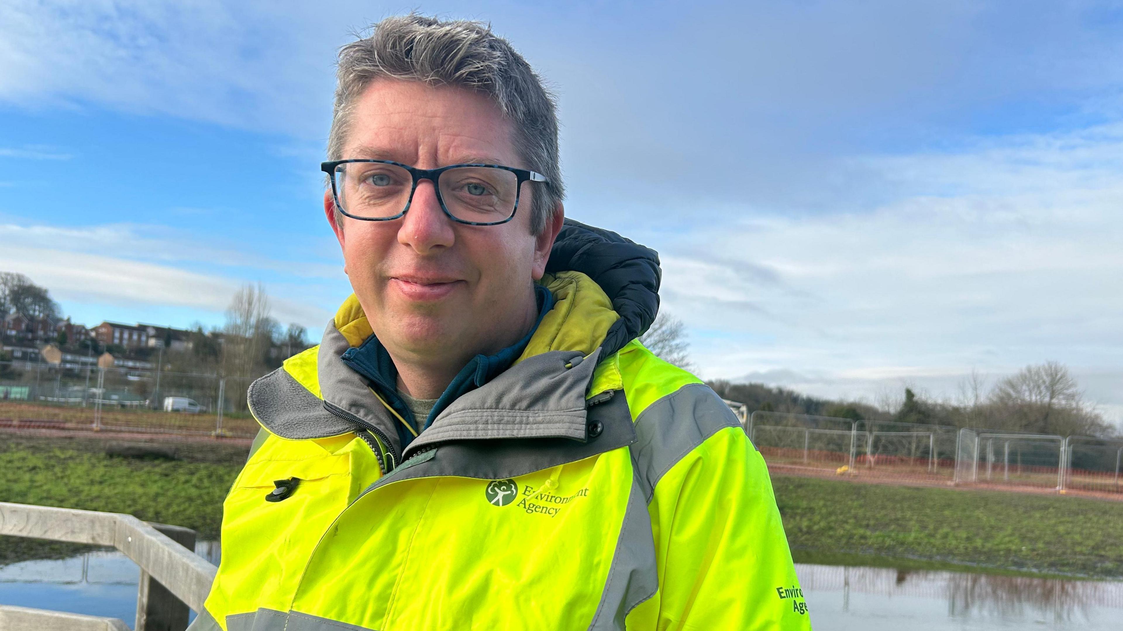 Andy Wallis smiling into the camera in front of the River Avon. He is wearing a hi-vis jacket