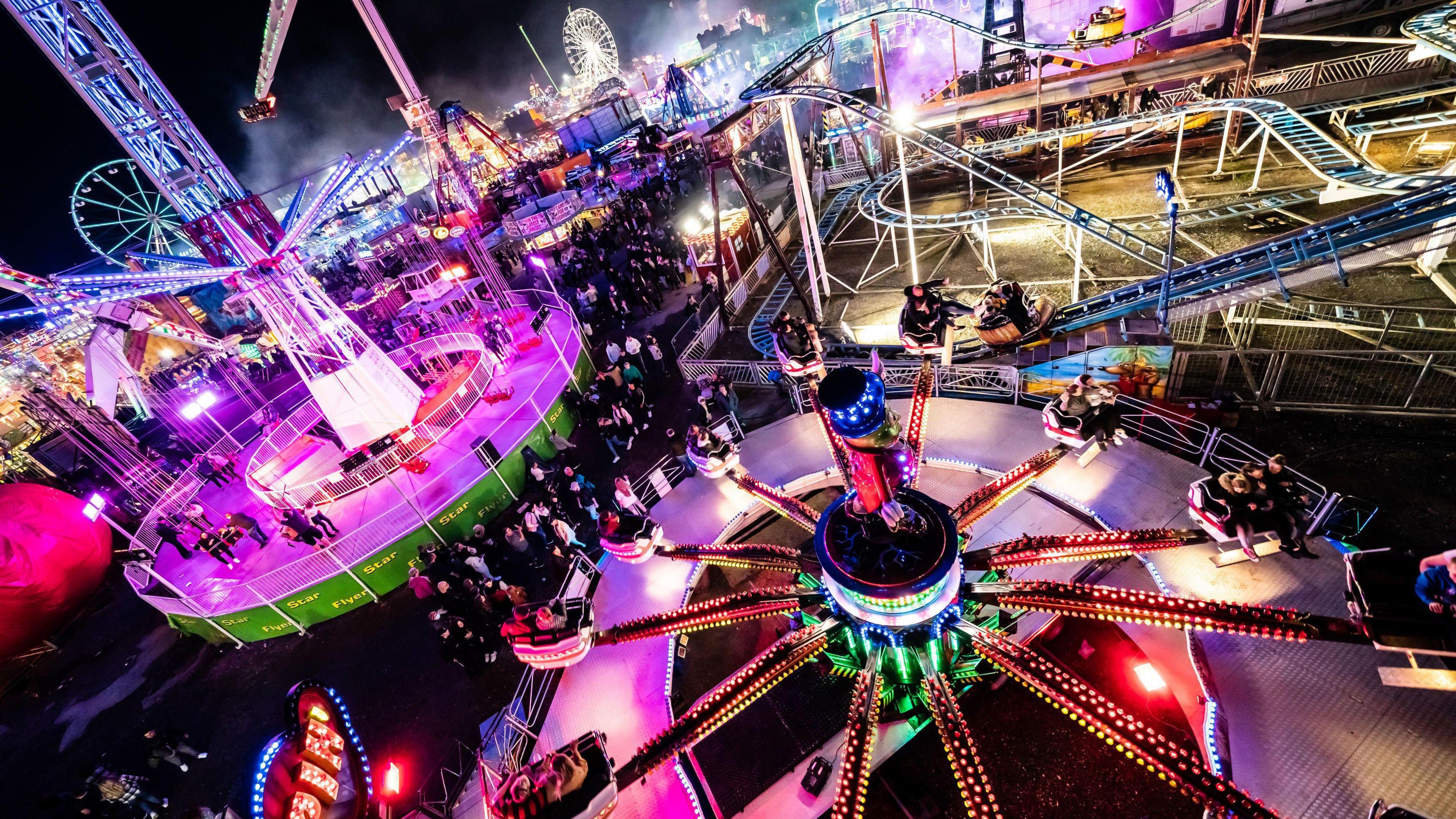 Colourful rides and a rollercoaster lit up against the night sky at Hull Fair.