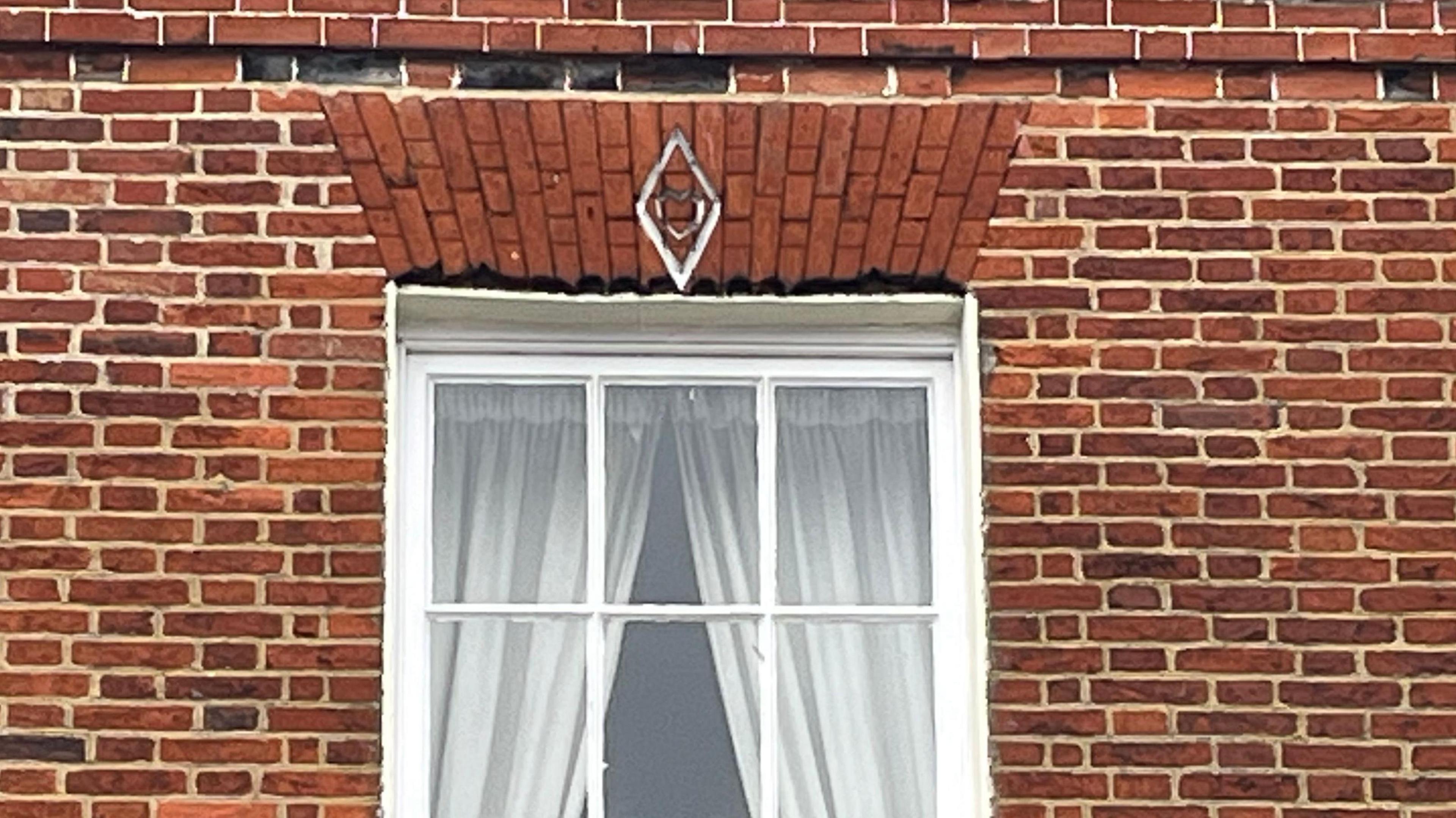 Close up view of a window within a brick wall. Above the window is a white mark depicting a heart within a diamond.
