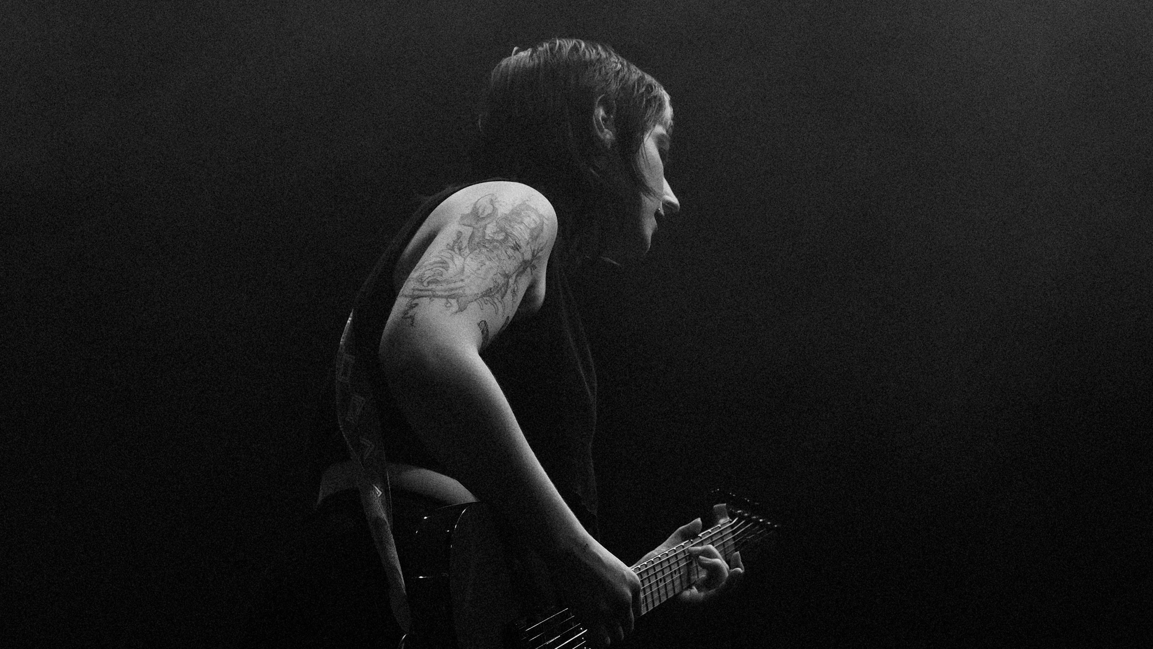 Black and white image of woman play guitar. She has tattoos on her arm. 