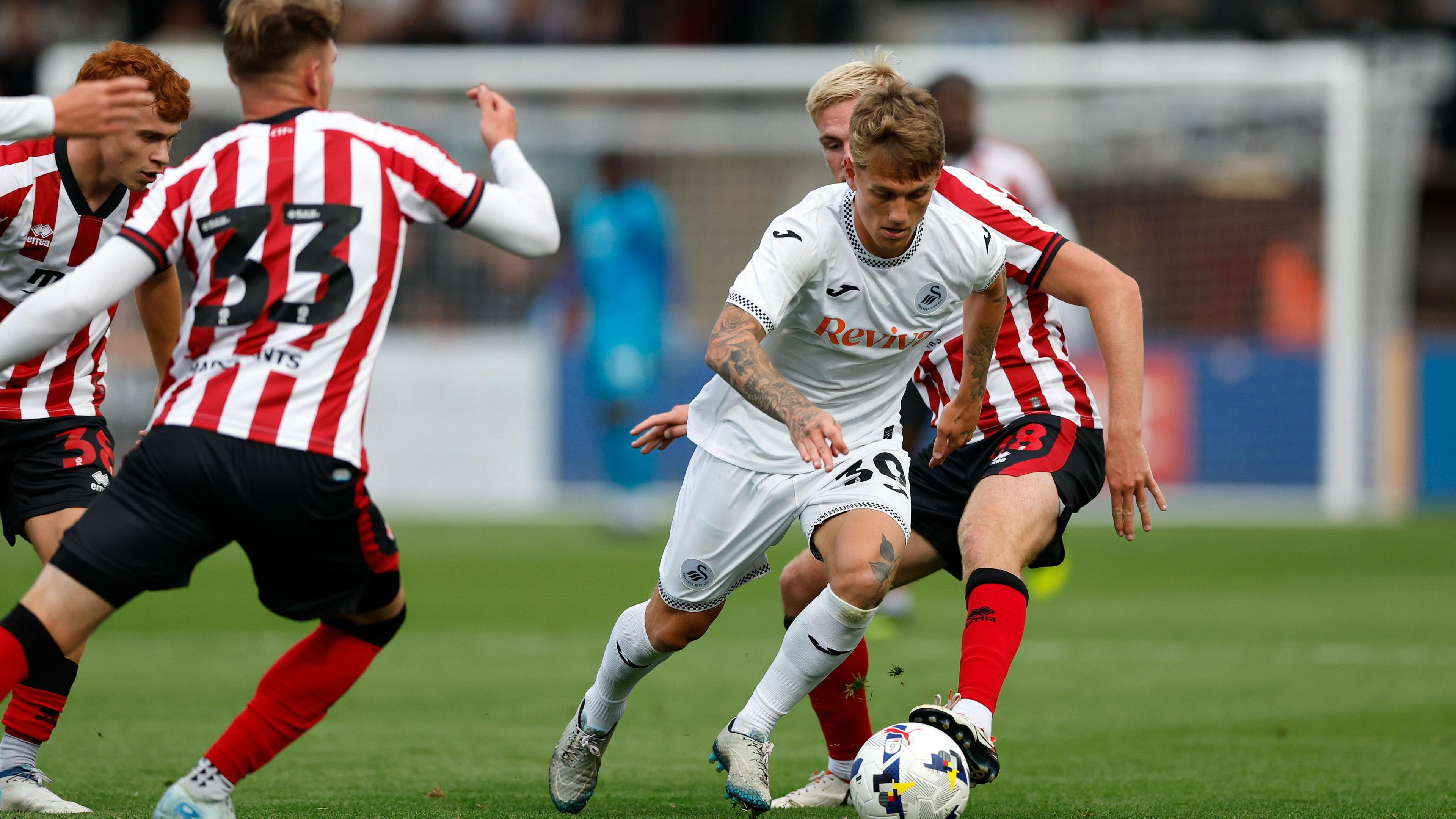 Ethan Galbraith dribbles past two Cheltenham players during pre-season