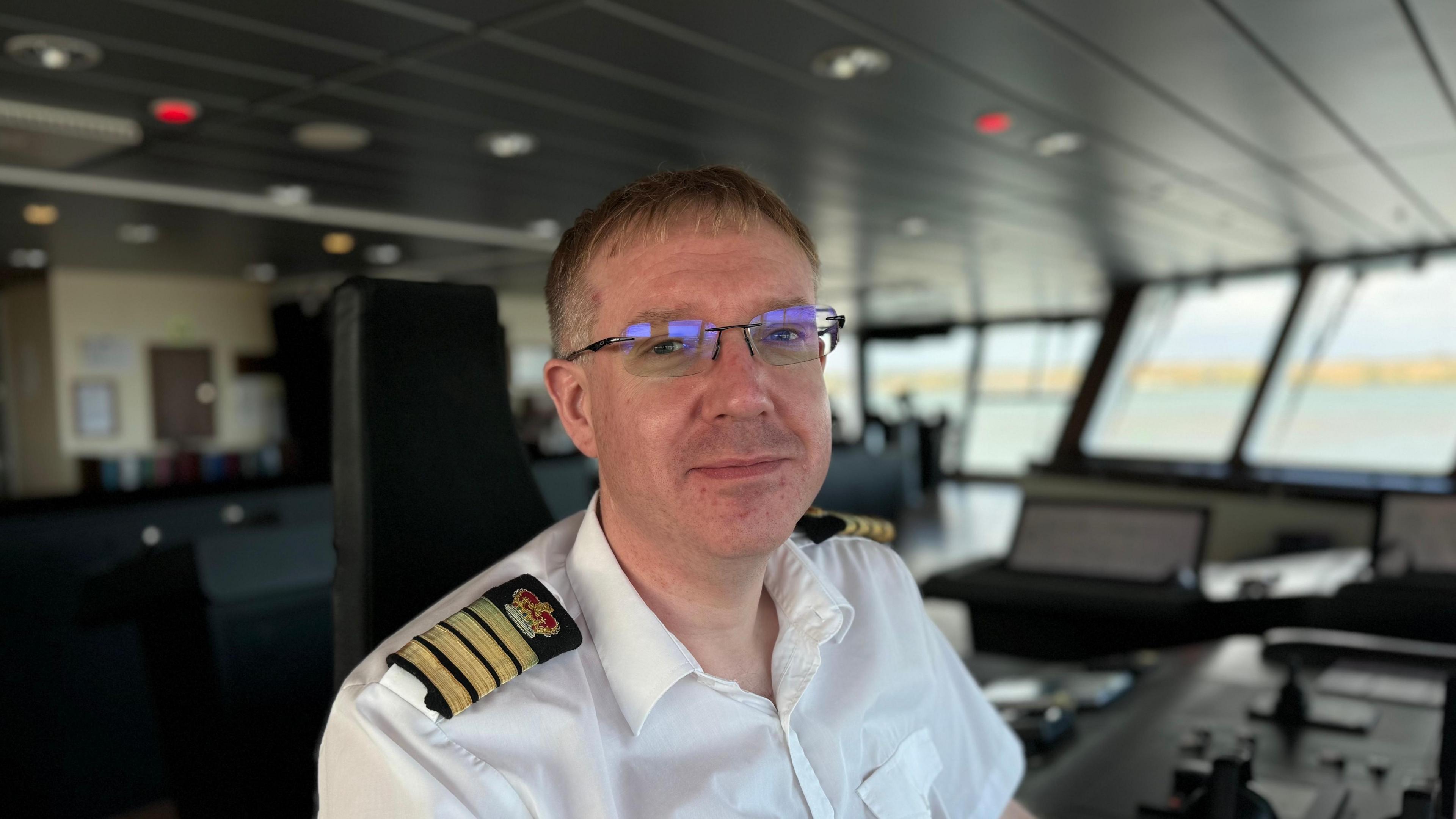 Captain Ralph Stevens looking at the camera. He is sitting in front of several computer monitors and wearing a white shirt and glasses.