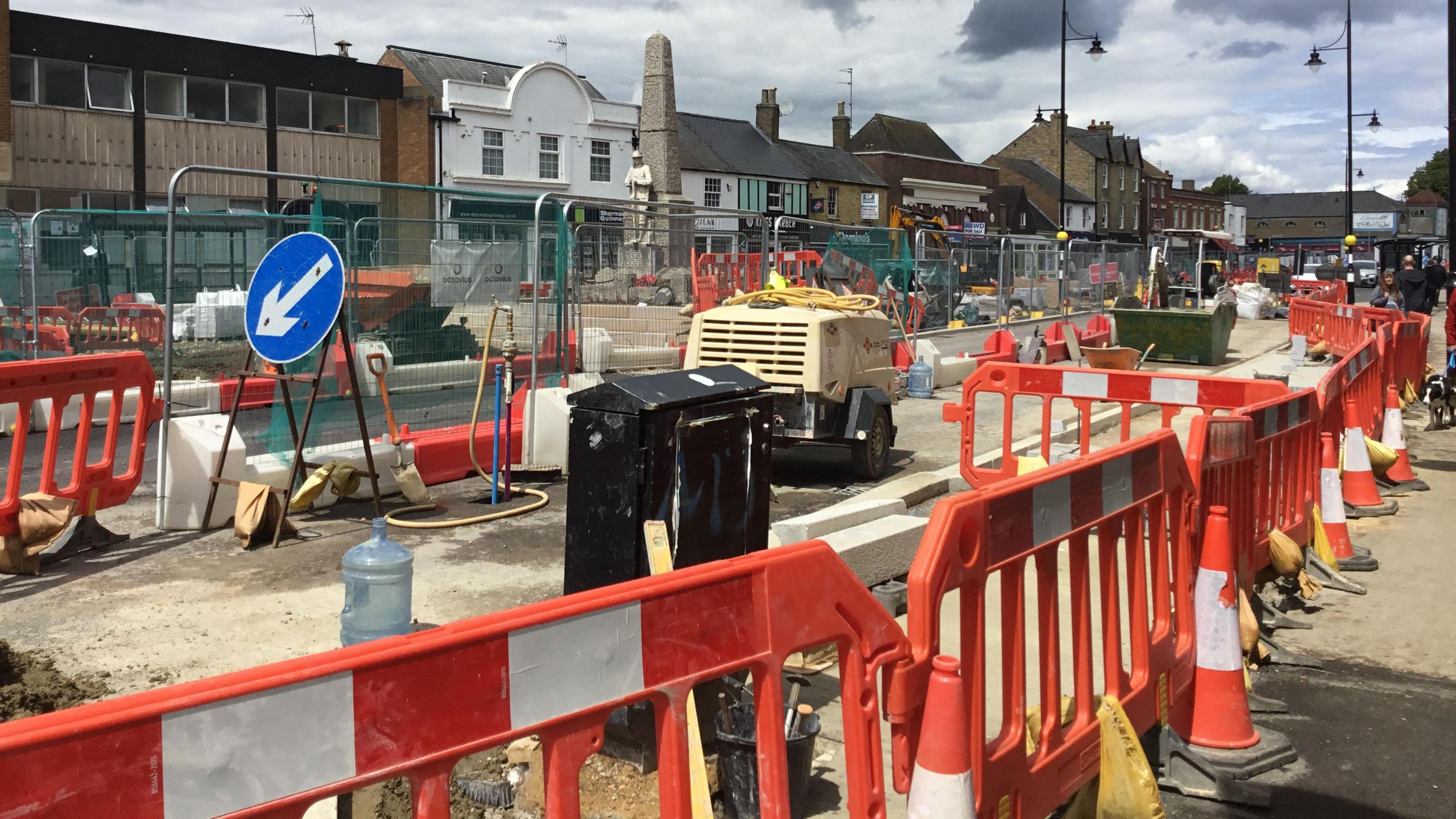 High street with colourful orange and white barriers, heavy machinery on the street, and shops either side